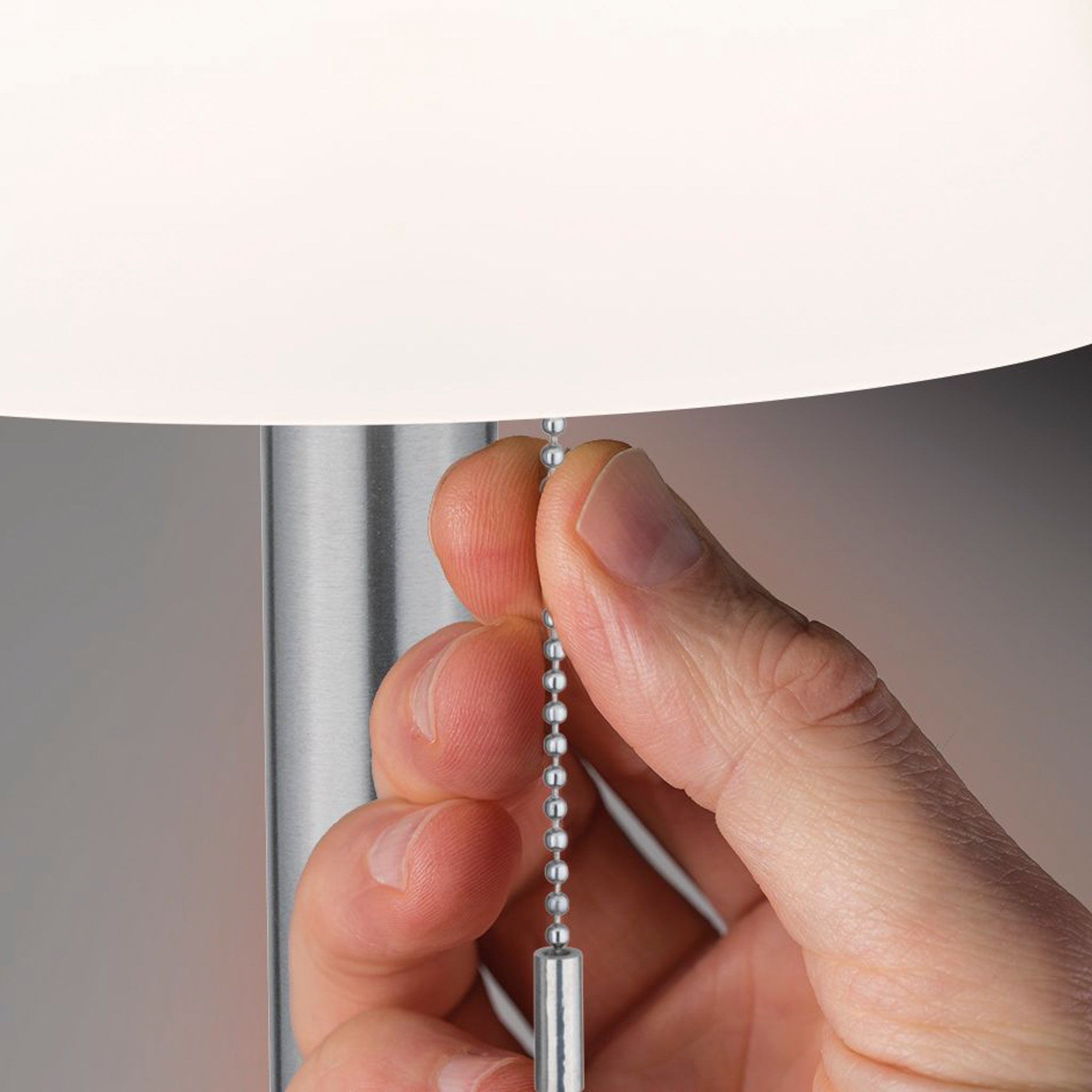 Close-up of a hand pulling a chain to turn on the Paulmann Outdoor Lillesol 0.8W LED Solar Table Lamp, featuring a white shade and stainless steel base, ideal for outdoor table luminaire setups with its 3-step dim feature.