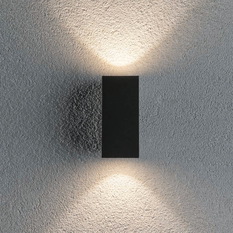 The Paulmann Outdoor Flame 6.6W LED Dual Output Wall Light in anthracite showcases a minimalist design with a rectangular black fixture that uses LED technology to create upward and downward lighting effects on a textured surface.