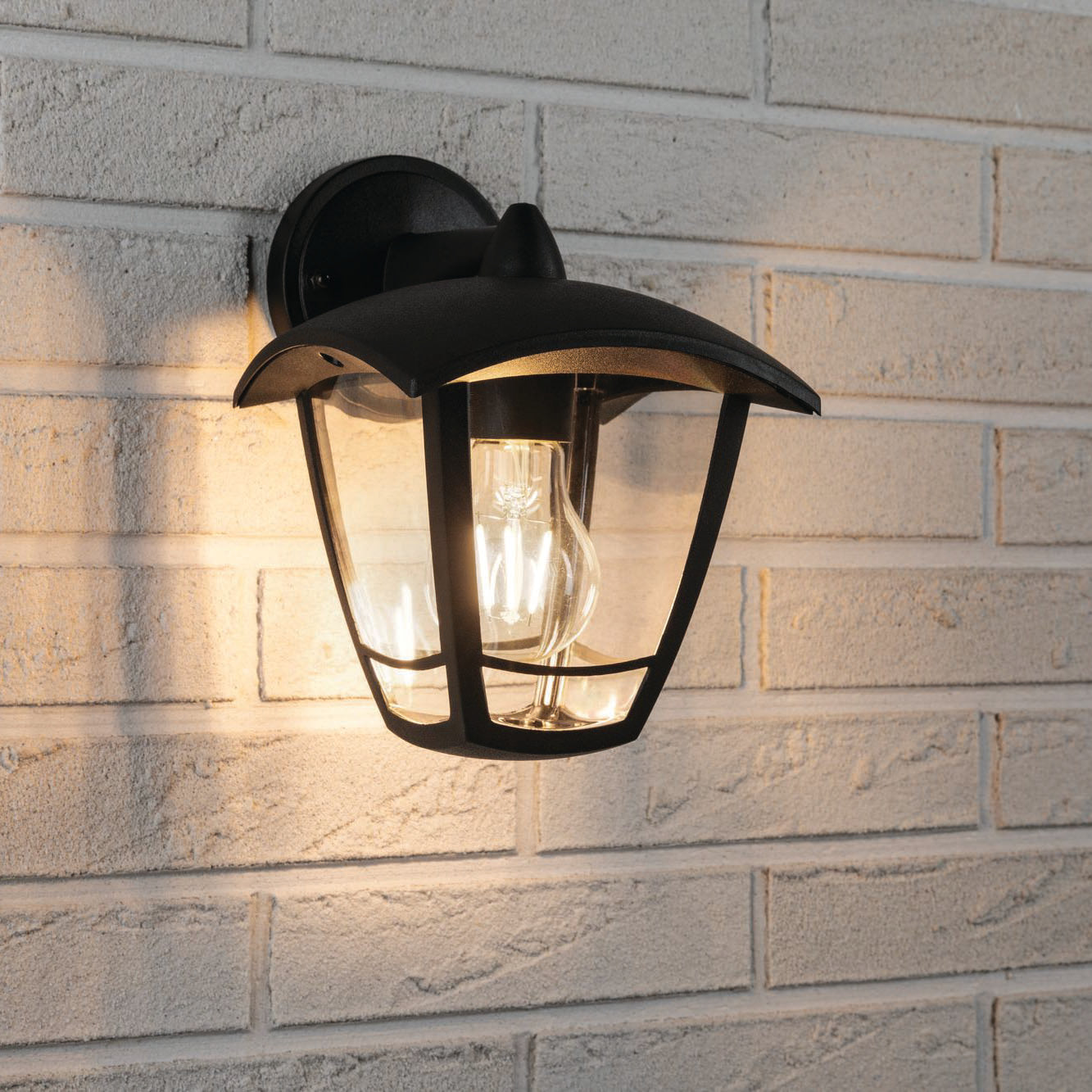 The Paulmann Outdoor Classic 12W LED Wall Light in Black features an anthracite-colored frame, illuminating a white brick wall with its classic exterior luminaire style and splash-proof design.