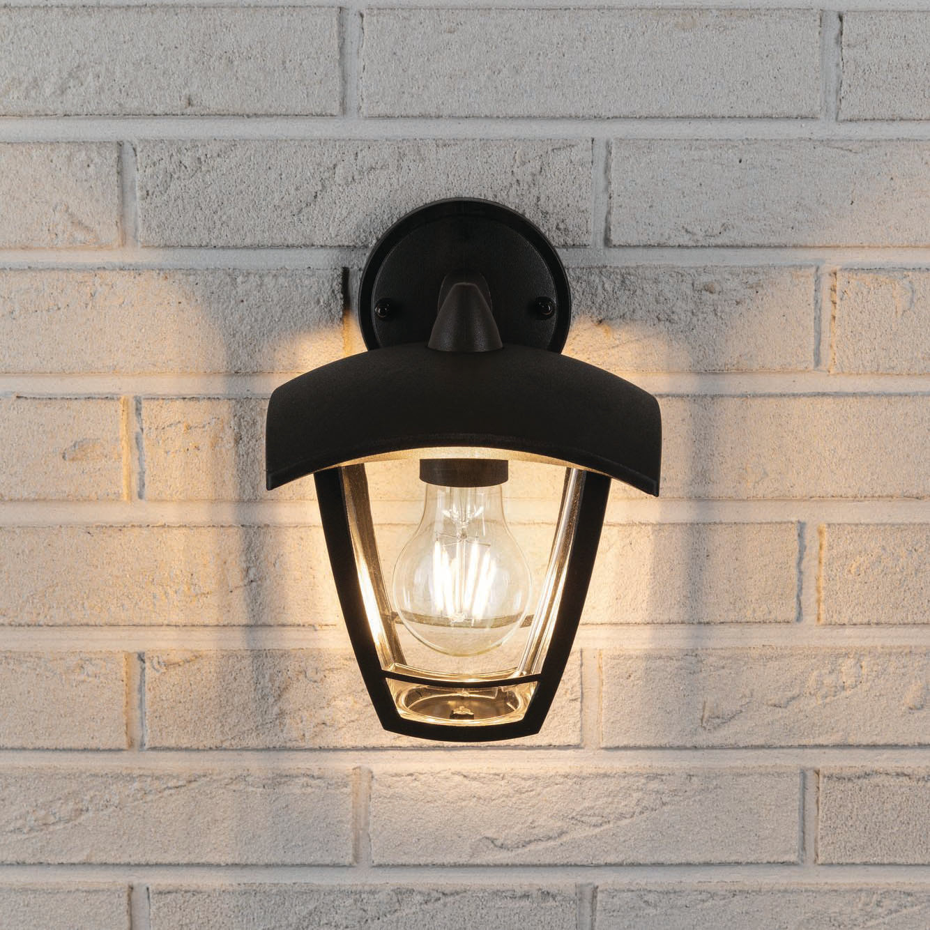 The Paulmann Outdoor Classic 12W LED Wall Light in black features a glowing bulb against a white brick wall, with an anthracite-coloured frame and a classic exterior luminaire design.