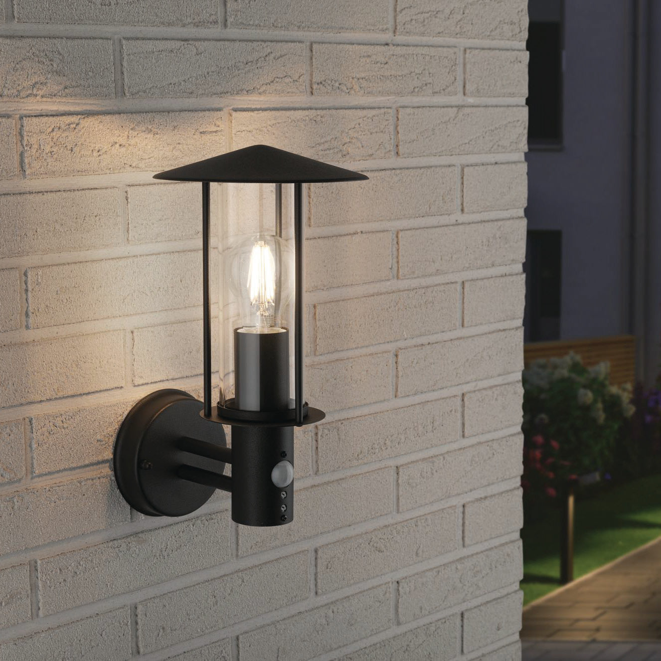 The Paulmann Outdoor Classic 15W LED Wall Light in Dark Grey stylishly illuminates your brick wall at night with its glowing light bulb, featuring a motion sensor for added security. With IP44 protection, it is designed to withstand the elements while enhancing your outdoor space.