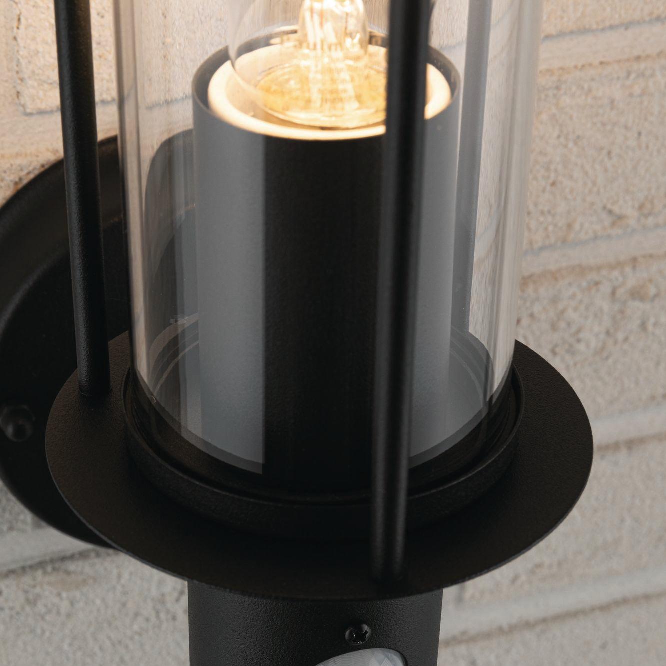 Close-up of the Paulmann Outdoor Classic 15W LED Wall Light in dark grey, featuring a sleek design with IP44 protection and motion detection capabilities. The visible bulb is elegantly enclosed within a glass cover, enhancing its aesthetic appeal as it stylishly integrates into the brick wall setting.