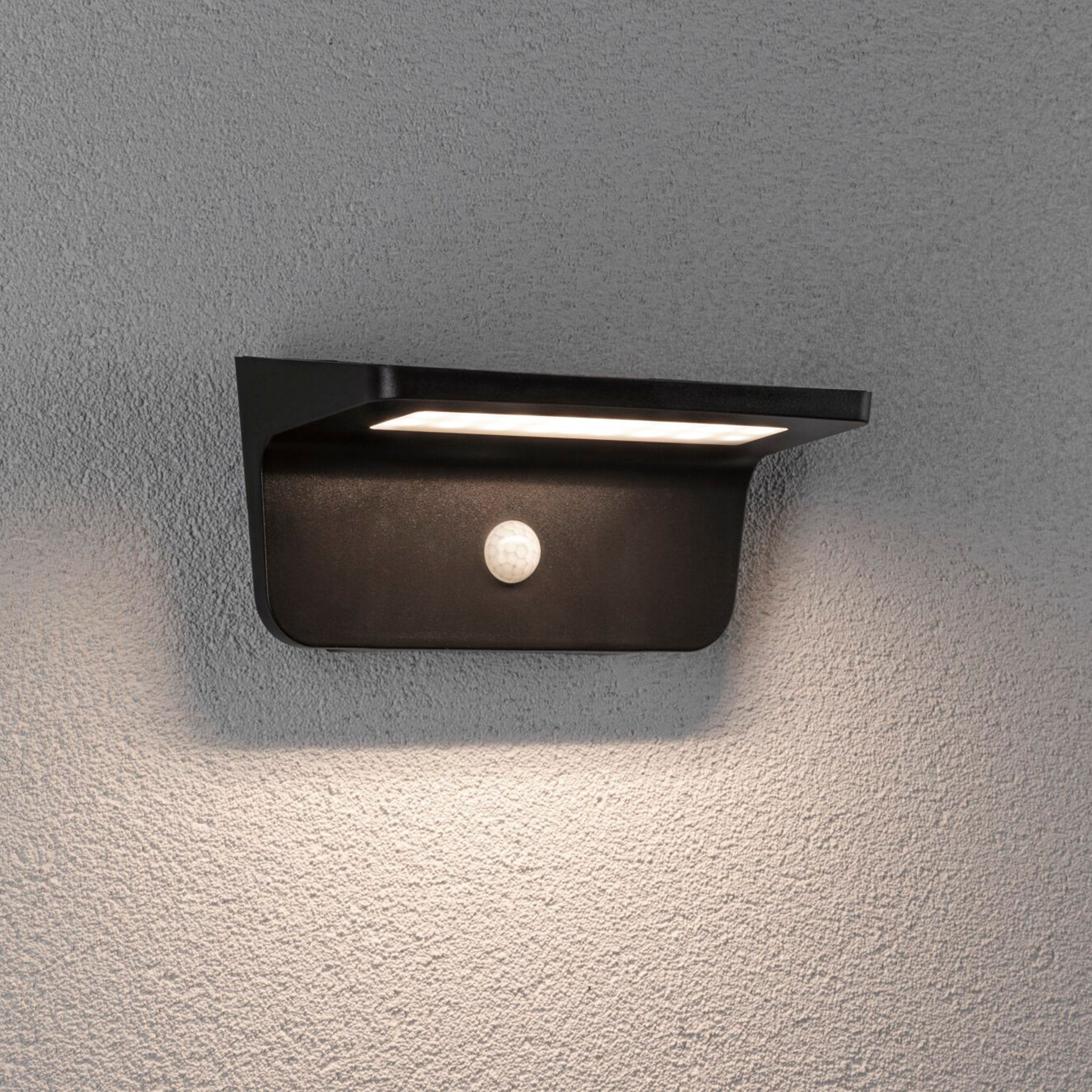 The Paulmann Outdoor Cyrus 5W LED Solar Wall Orientation Light with motion detection is mounted elegantly on a textured gray exterior wall, offering IP44 protection to ensure durability and performance in various weather conditions.