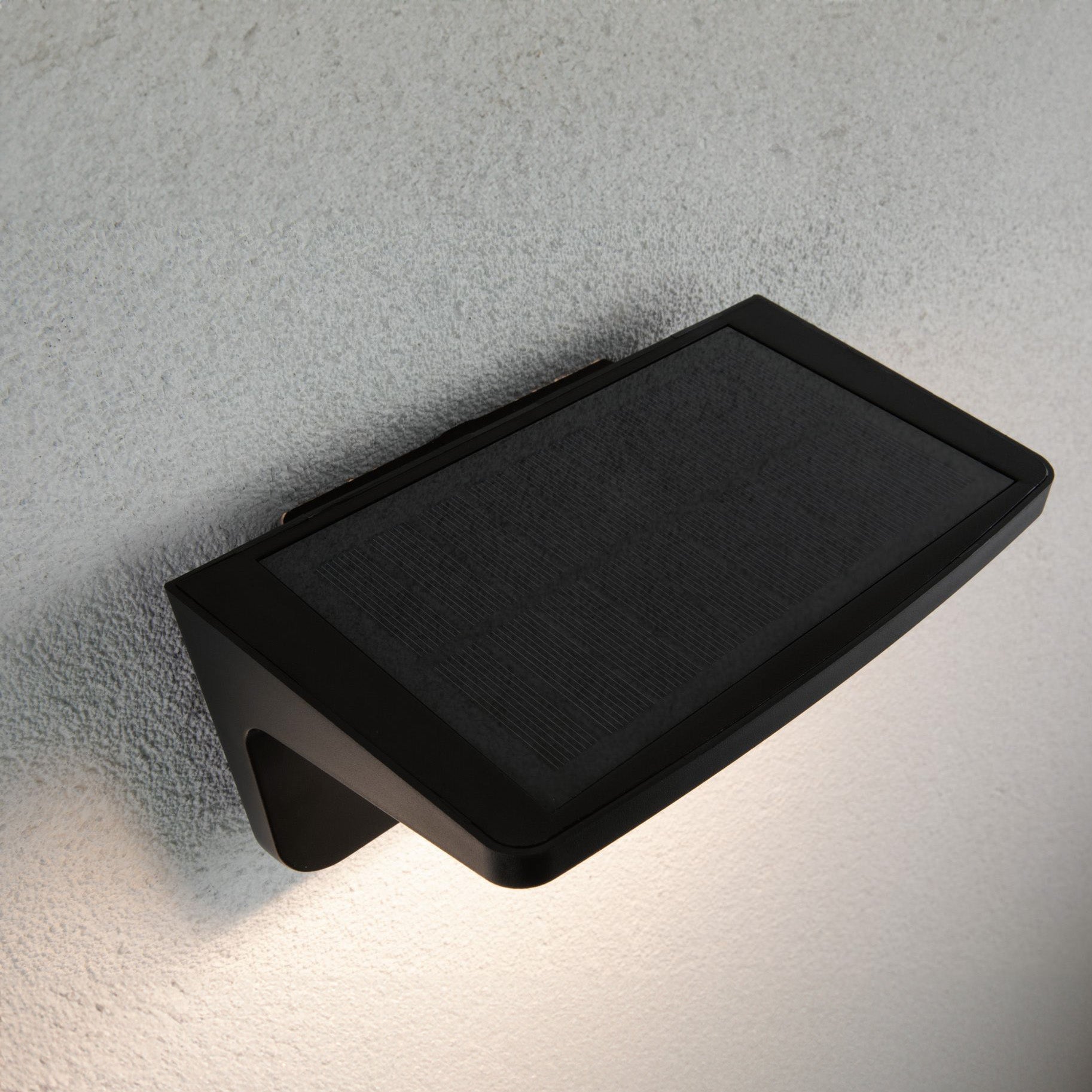 The Paulmann Outdoor Cyrus 5W LED Solar Wall Orientation Light, featuring motion detection in anthracite, elegantly graces the textured white exterior wall with its energy-efficient illumination and IP44 protection.