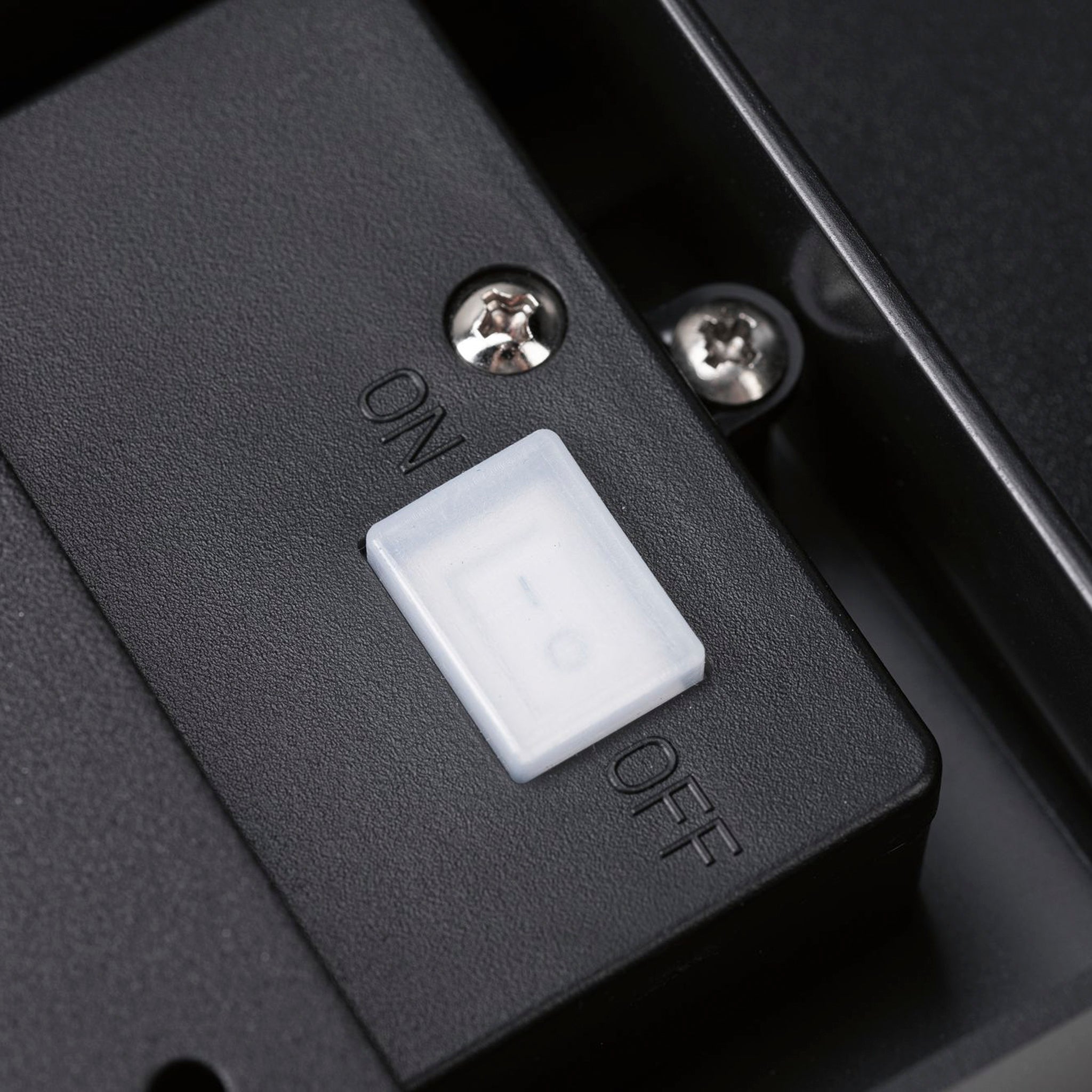 Close-up of a white on-off switch on the Paulmann Outdoor Cyrus 5W LED Solar Wall Orientation Light in anthracite, with screws visible nearby, highlighting its IP44 protection, making it ideal for exterior walls.