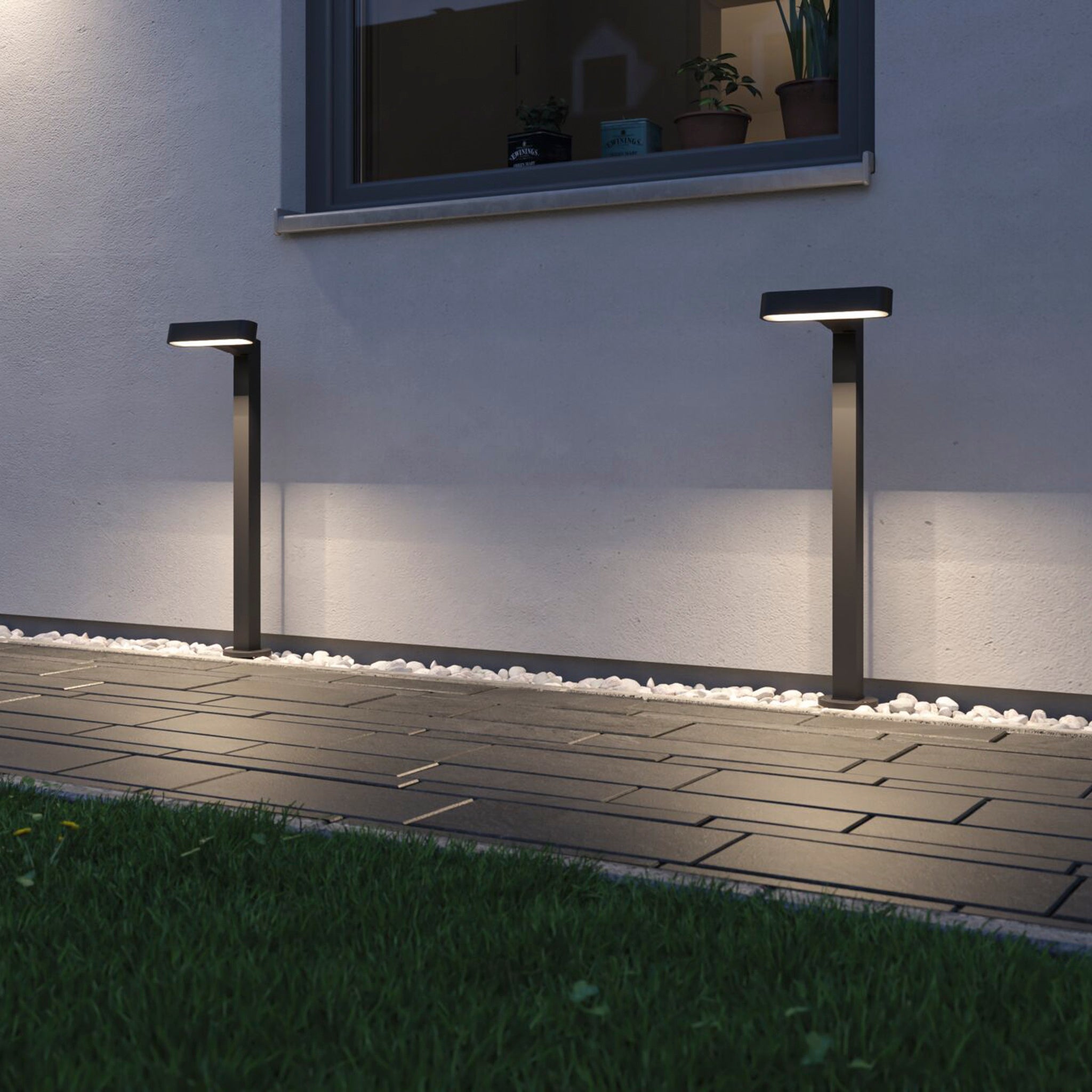 The Paulmann Plug & Shine Outdoor Ito 6W LED Horizontal Bollard in Anthracite lights up stone walkways and lawns at dusk, creating inviting garden paths with modern outdoor lighting.