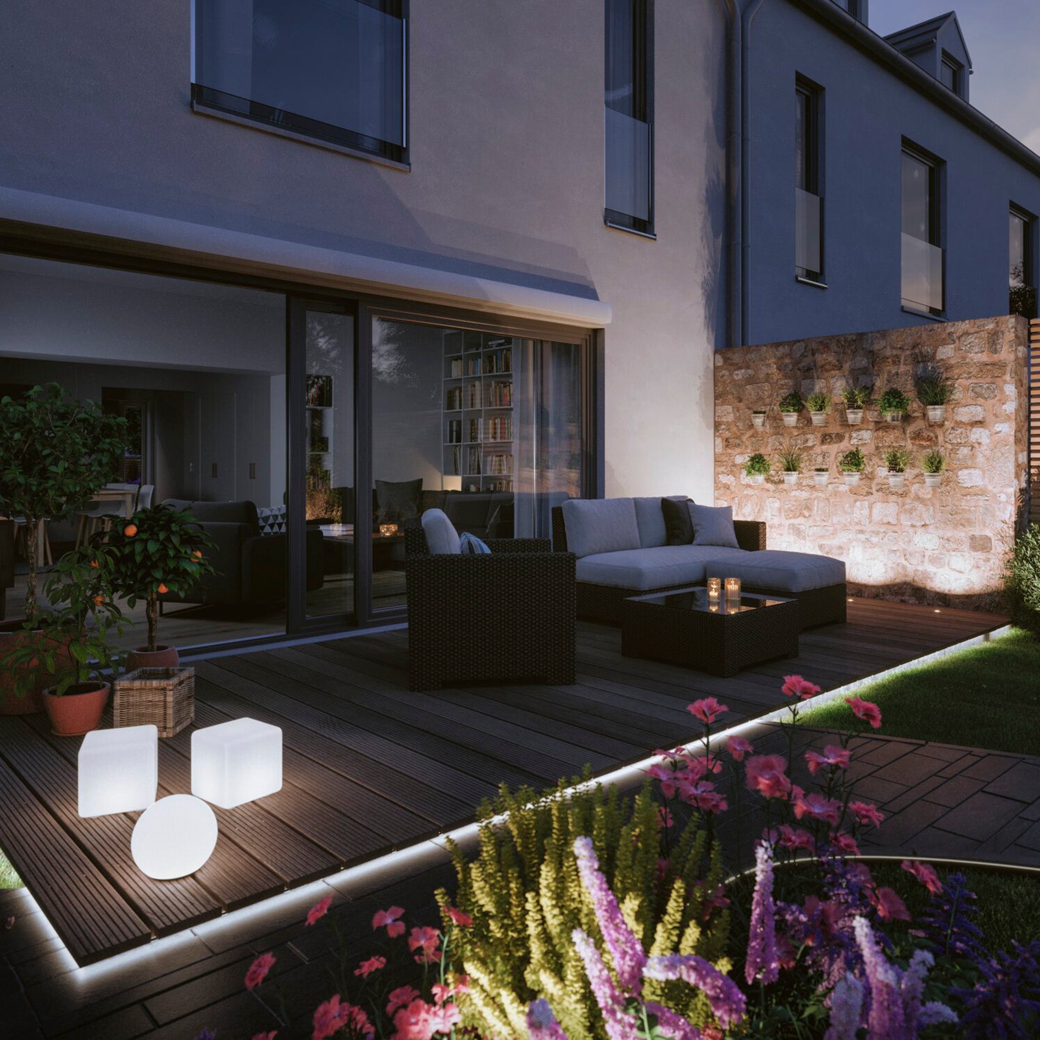 Modern patio at twilight featuring a weather-resistant sofa set, glowing Plug & Shine Outdoor 48W LED 10m Smooth Strip with Smart Home Zigbee 3.0 in RGBW lights with a tunable white function, potted plants, and a vertical garden on the stone wall.