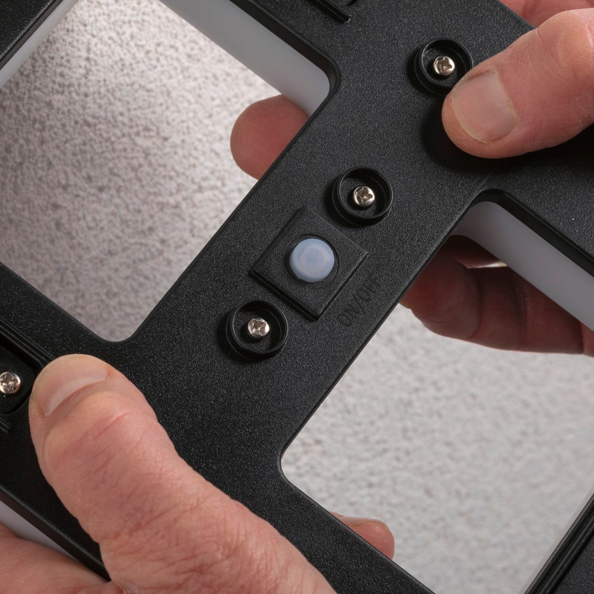 Hands adjusting a black wall mount bracket with screws on a textured surface, preparing to install the Paulmann Outdoor Solar House Letter A LED 0.2W with Replaceable Battery.