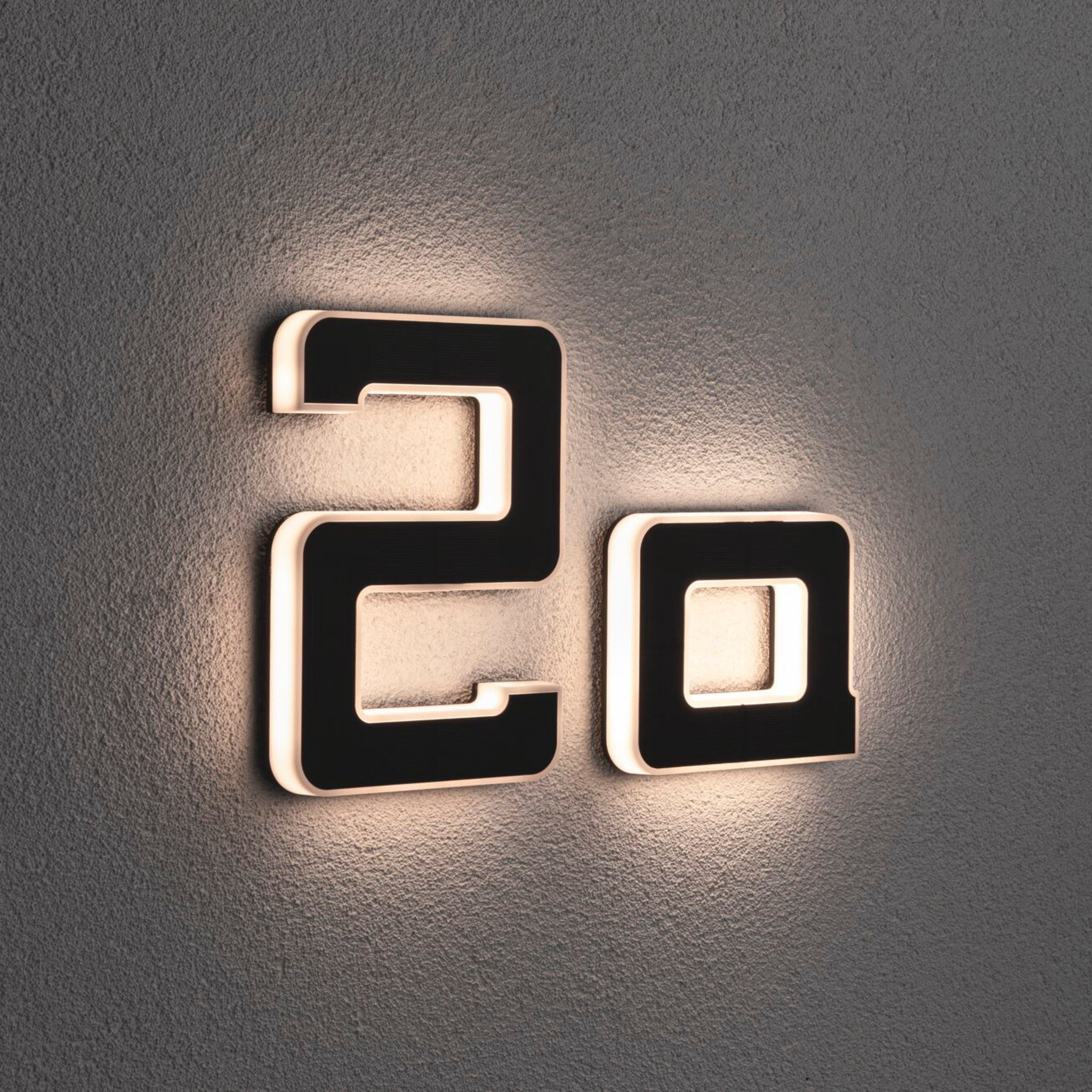 The decorative letter "A" from Paulmann gently illuminates a textured wall like an outdoor solar house luminaire, casting a warm light around its edges.