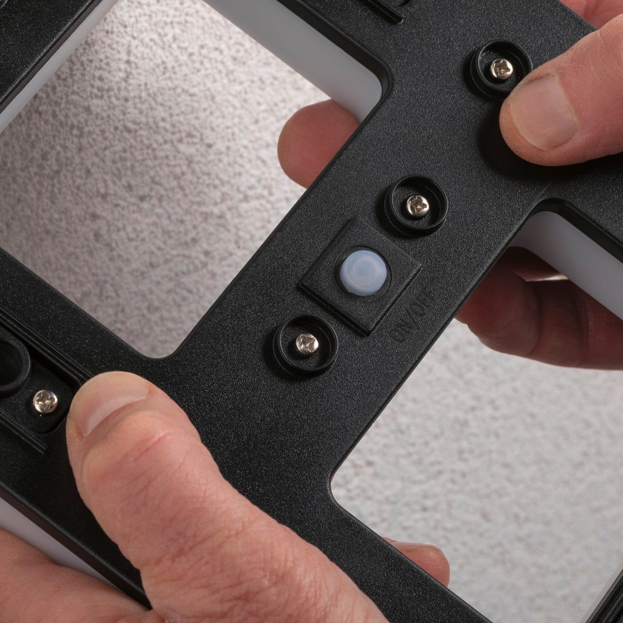 Hands adjusting a sleek black wall mount with screws on a textured surface, perfect for showcasing the Paulmann Outdoor Solar House Letter B LED 0.2W with Replaceable Battery.