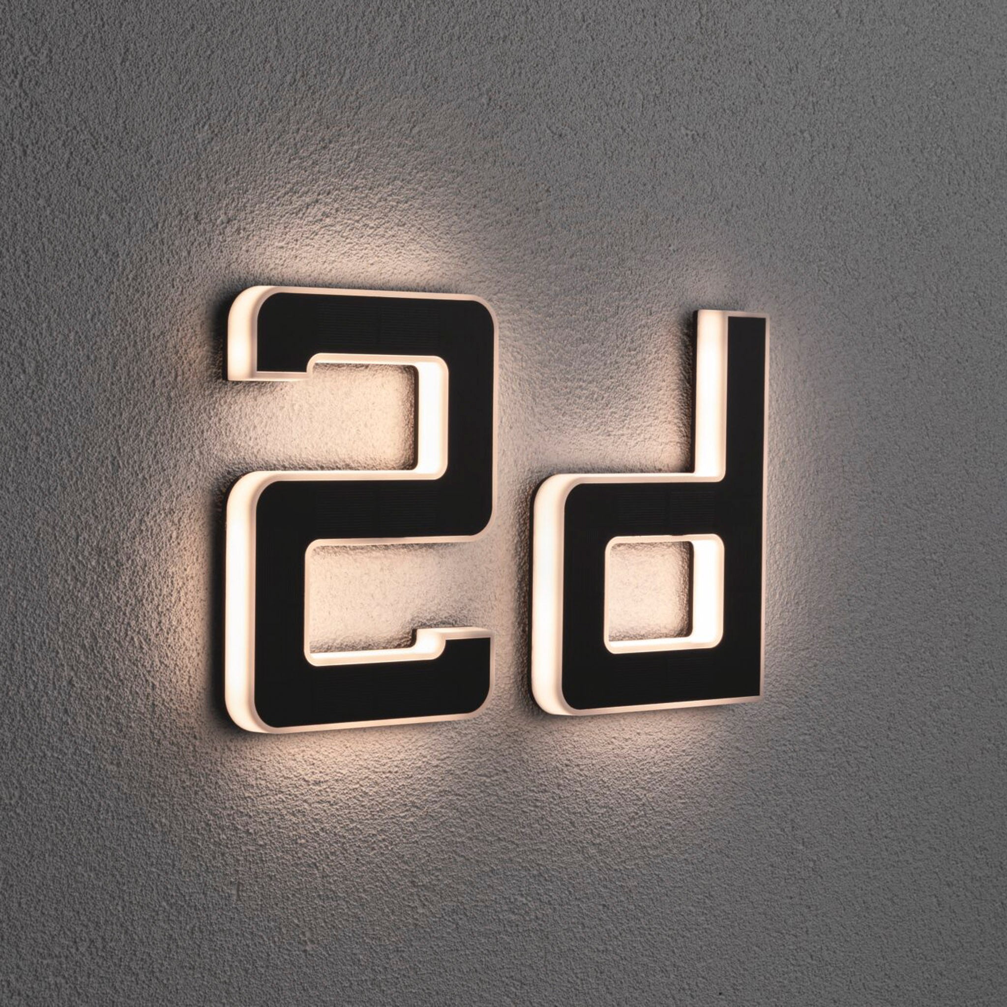 Wall-mounted "D" house letter luminaire by Paulmann, featuring a soft backlight on a gray textured surface and boasting a sleek solar-powered design with replaceable battery in black.