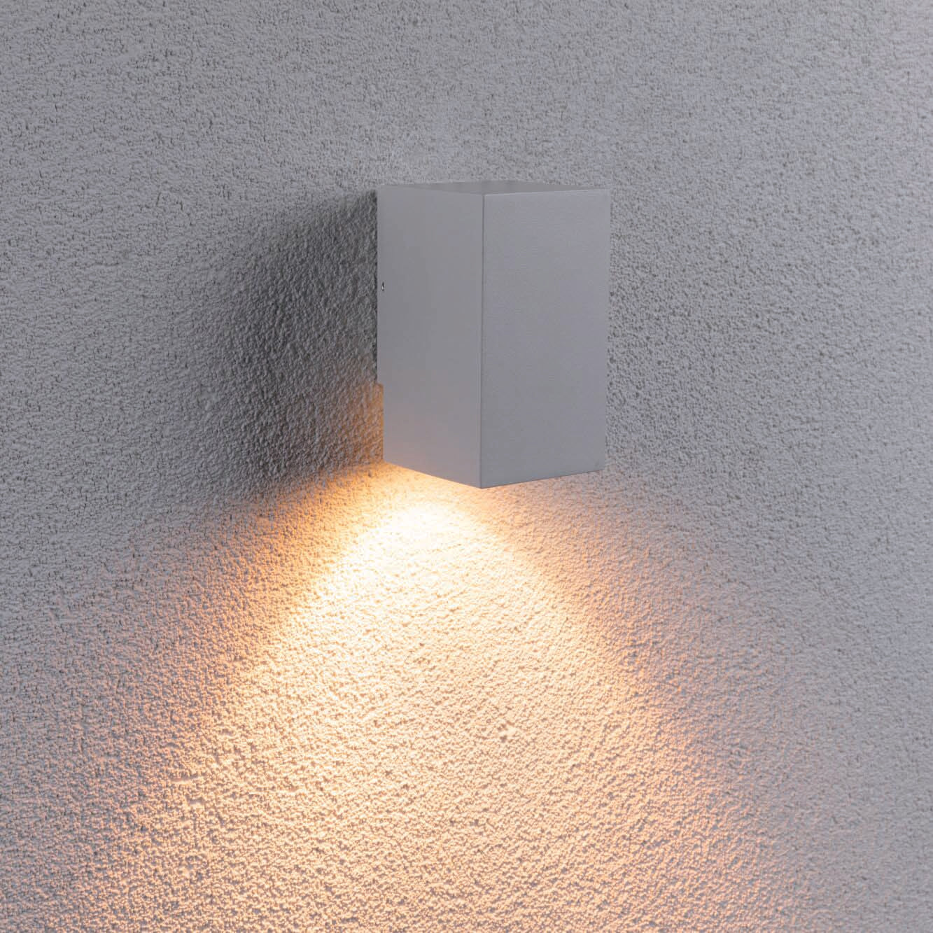 The Paulmann Outdoor Flame Insect Friendly 5.2W LED Single Output Wall Light in White efficiently casts warm light on a textured wall, embracing the night with its insect-friendly glow.