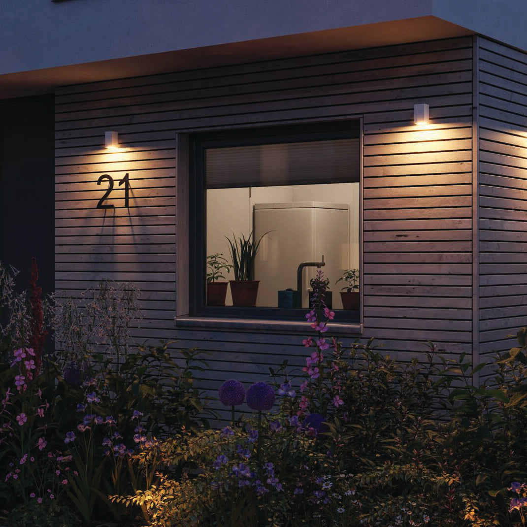 The wooden exterior of the house warmly glows under the glow of Paulmann's Outdoor Flame Insect Friendly 5.2W LED Wall Light in White. Positioned with care amid a lush night garden, these lights are designed to be gentle on insects, creating a serene and inviting atmosphere without disturbing nature's nocturnal visitors.