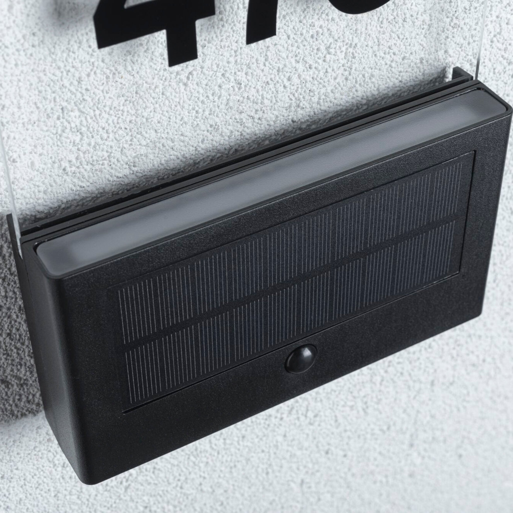 A stylish anthracite solar-powered wall light with motion detection and insect-friendly illumination, beautifully mounted on a textured white wall.