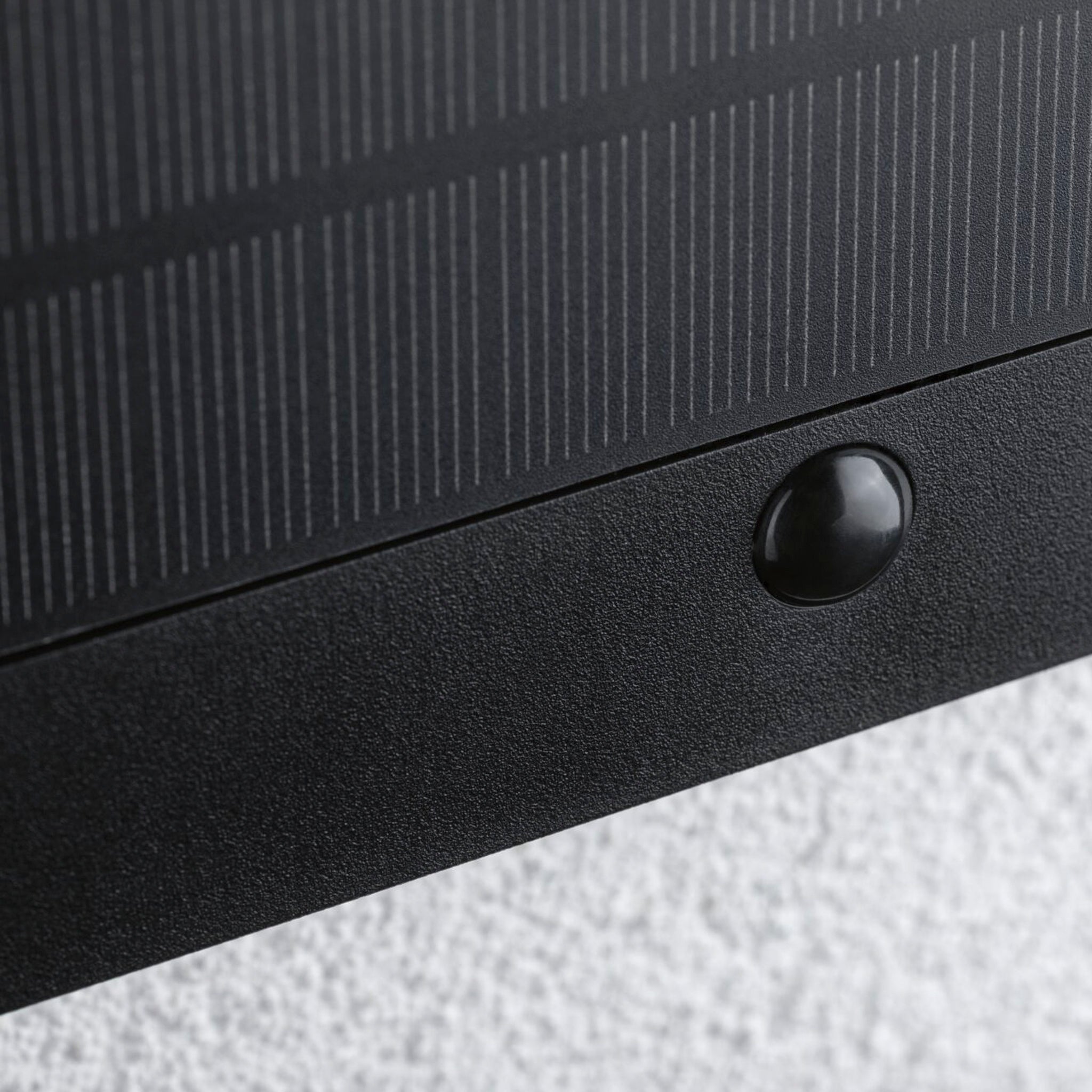 Close-up view of the Outdoor Neda Solar House Number 1W LED in Anthracite with Motion Detection & Insect Friendly Lumination, featuring a small black rubber stopper underneath, mounted on a textured surface and providing power to an illuminated house number luminaire with an integrated dusk sensor.