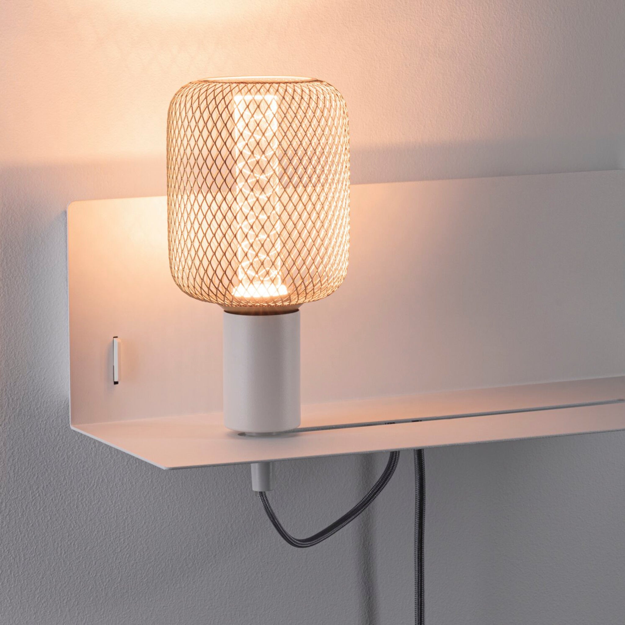The Paulmann - Devara 40W Wall Mounted Lamp in White Matt emits warm light from its modern design, featuring a mesh shade and a convenient integrated shelf along with a USB port.
