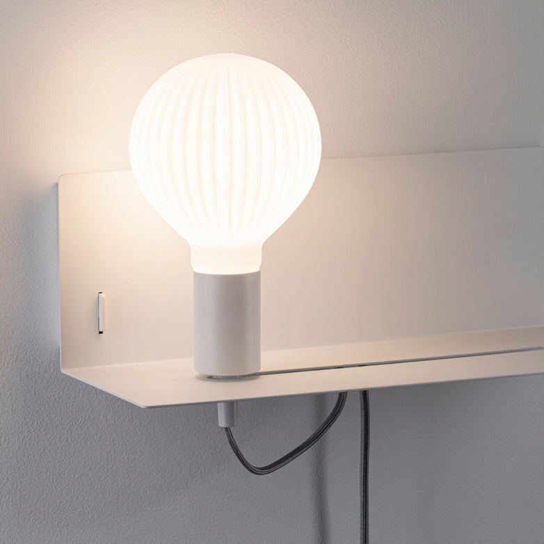 Introducing the Paulmann - Devara 40W Wall Mounted Lamp in White Matt, featuring a minimalist design with a round, ribbed glass bulb set on a sleek integrated shelf. The lamp includes a stylish black cord and a convenient USB-C charging port for enhanced functionality.