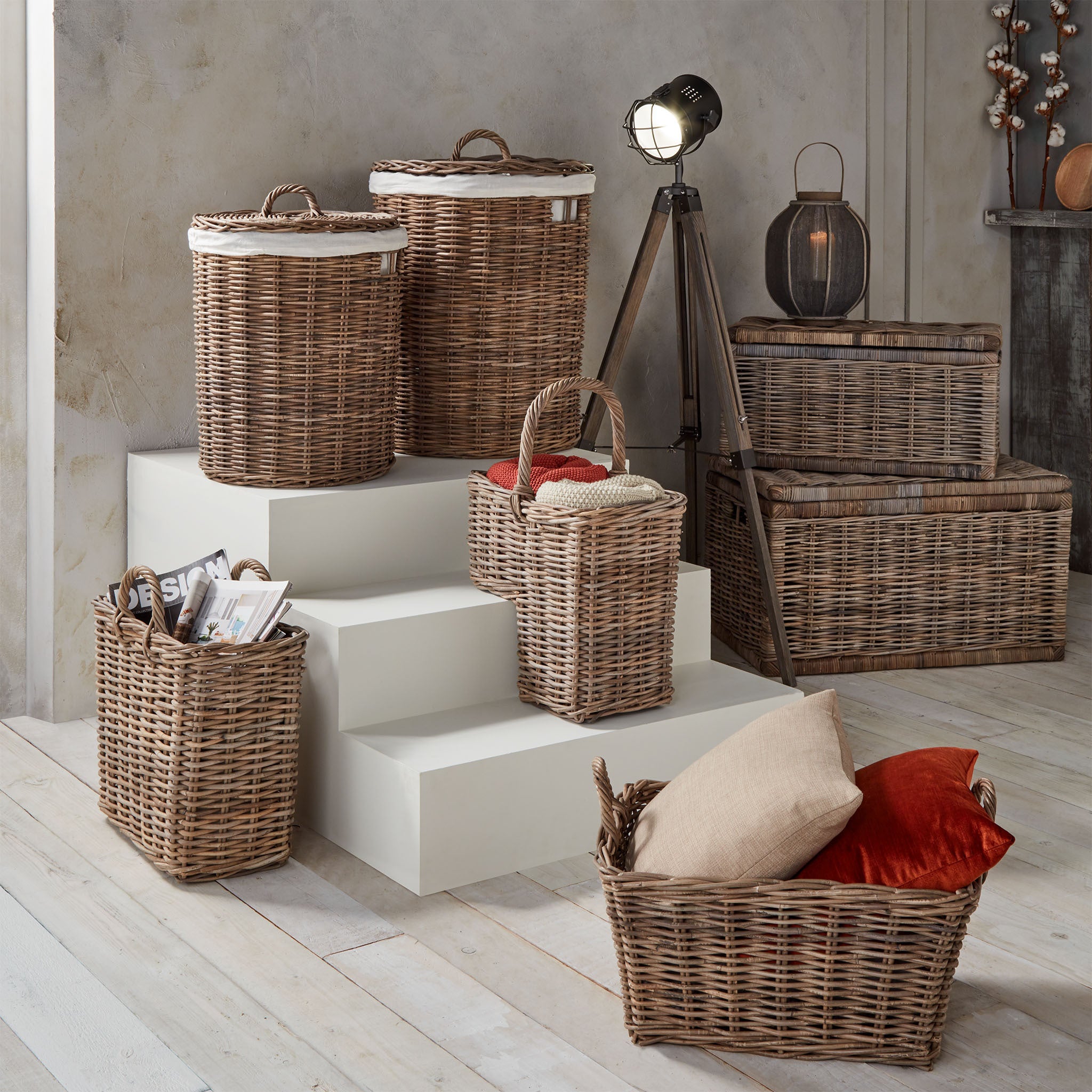 A room features Pacific Lifestyle's Bali Grey Kubu lined linen baskets on white steps and a wooden floor, filled with pillows and magazines, exuding a warm rustic decor.