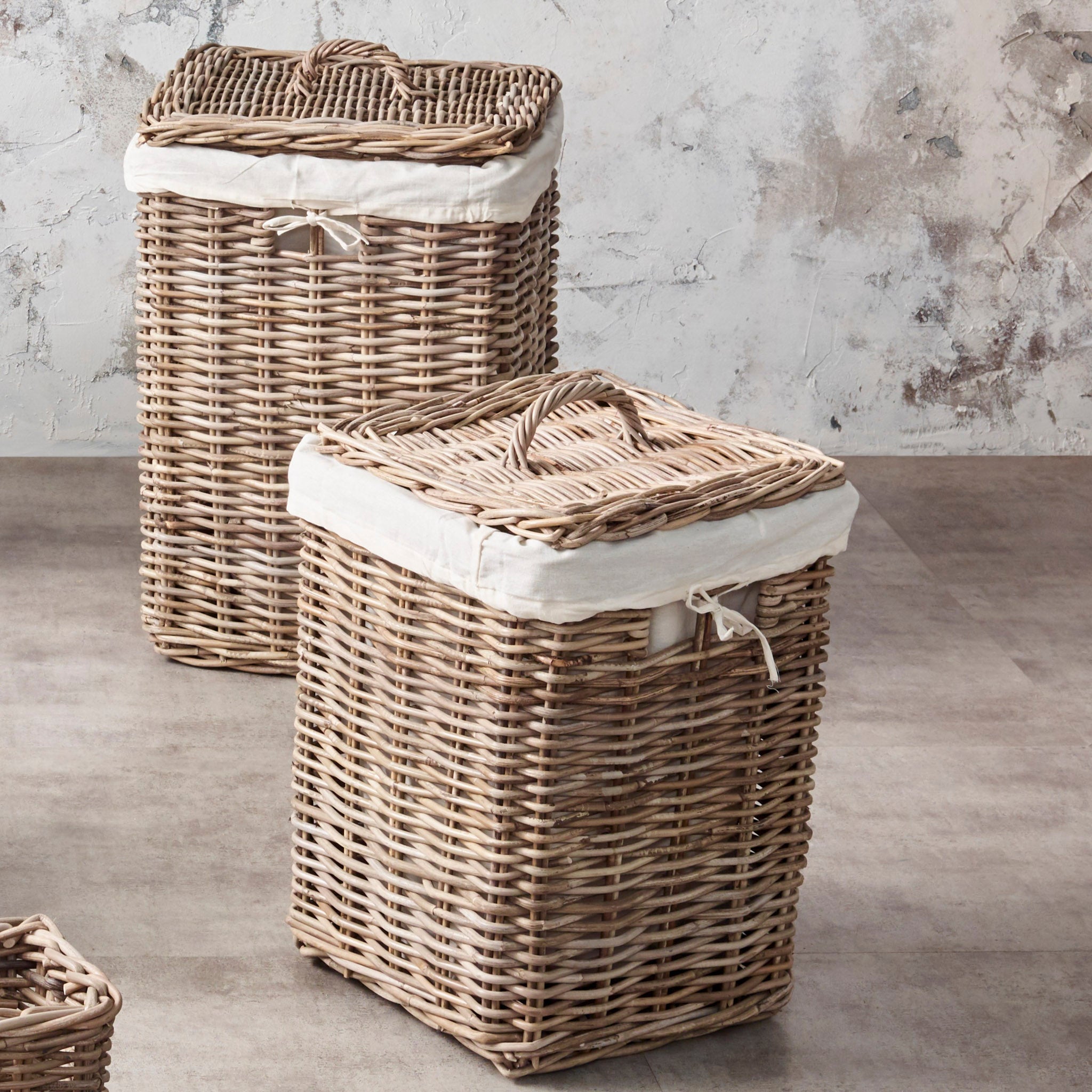 Two square wicker linen baskets with lids and white fabric lining from the Pacific Lifestyle - Bali Grey Kubu Set rest on a textured floor against a light wall.