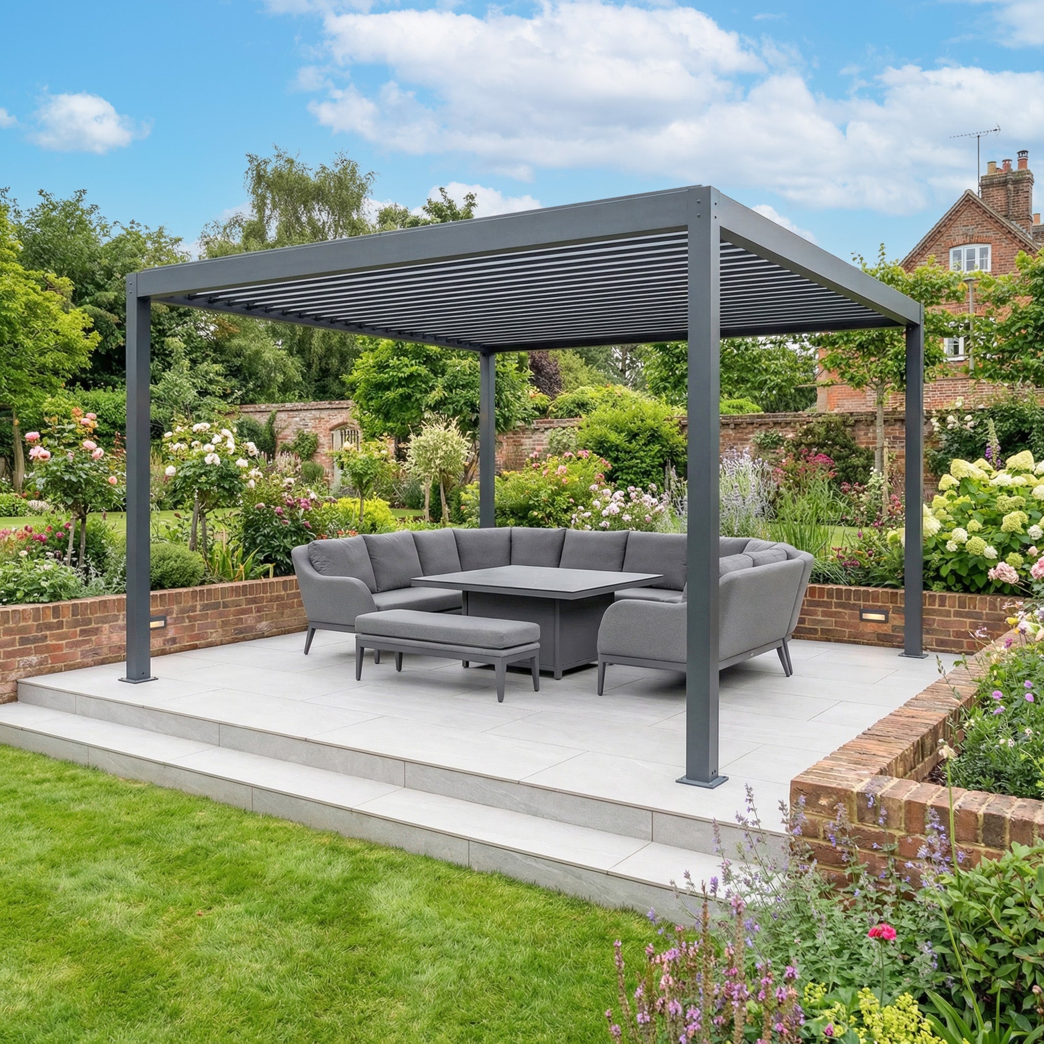 The PergoSTET Plus Frame Only 4m x 4m Square Pergola with LED Lighting in Grey stands in a landscaped garden with vibrant flowers and greenery, offering a modern outdoor retreat.