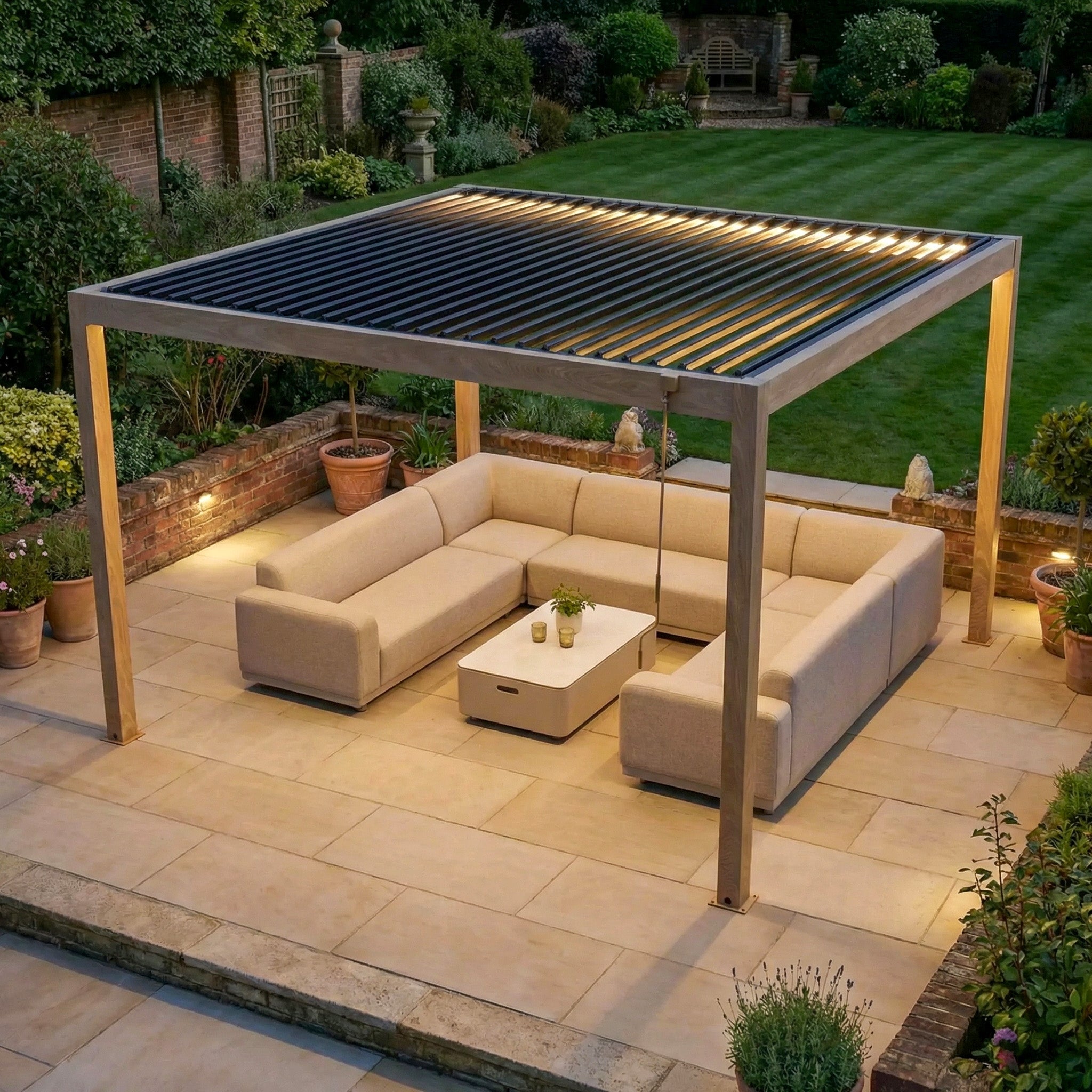 The PergoSTET Plus Frame Only 4m x 4m Square Pergola with LED Lighting in Wood Effect elevates this patio, paired with beige outdoor sofas and a table on tiled flooring, beautifully lit and set within a lush garden.