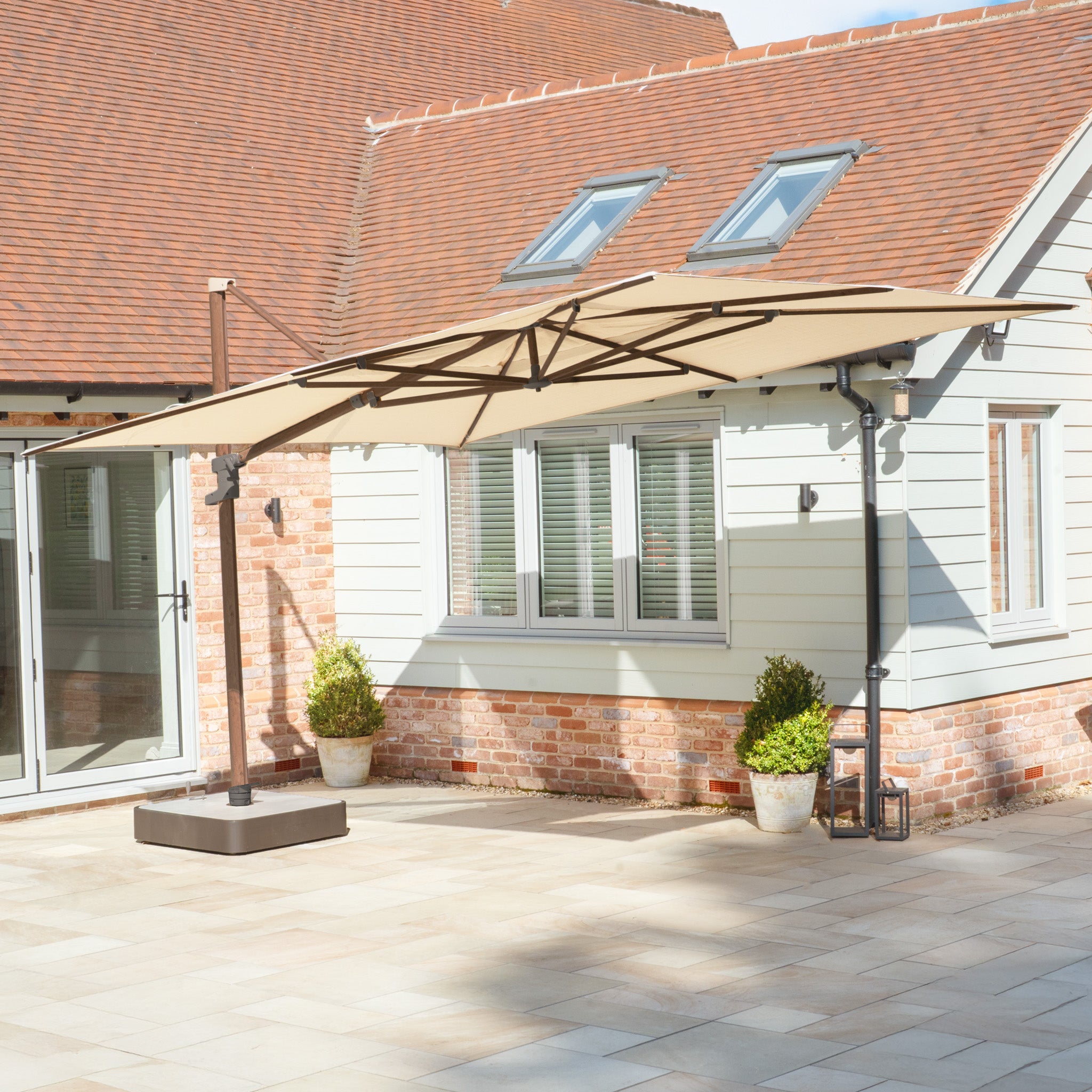 The Finca 4m x 3m Cantilever Parasol in Walnut provides stylish sun protection, shading your patio or garden area beside a modern home with potted plants.