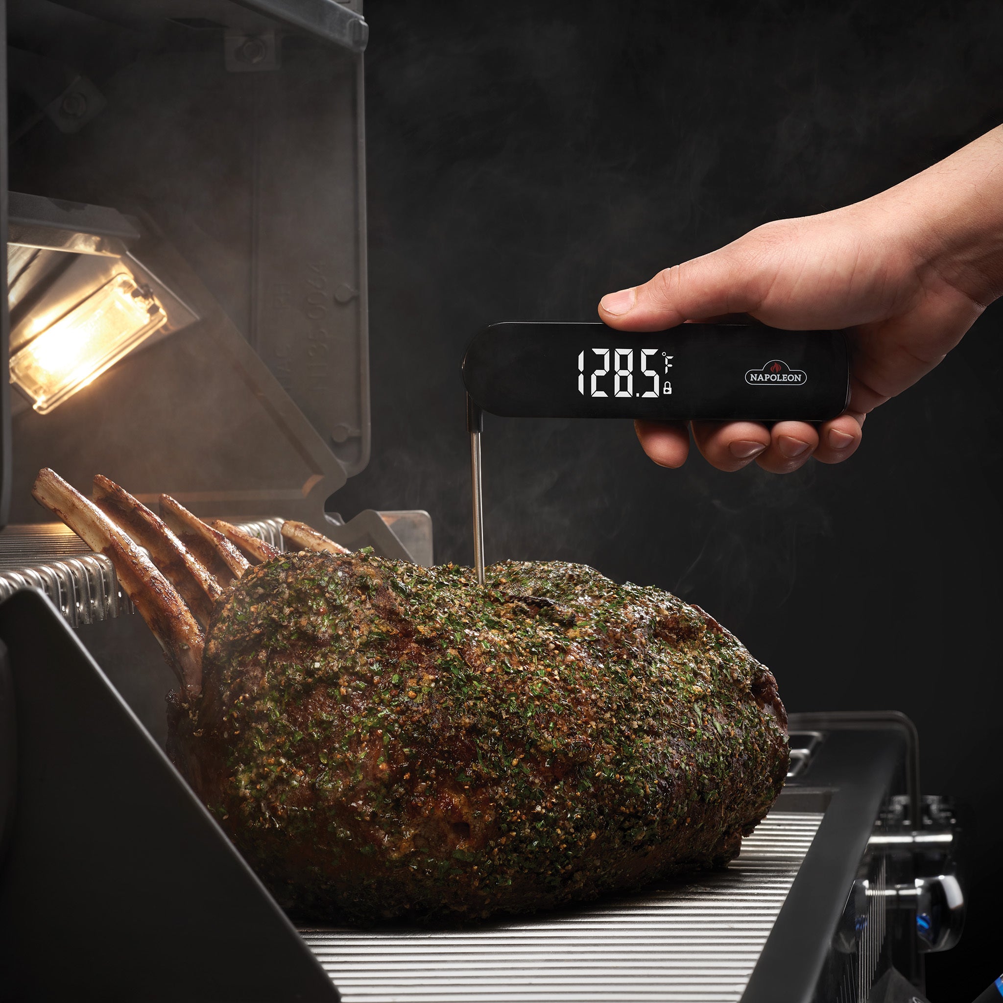 A hand uses the Napoleon - Fast Read Thermometer to check the internal temperature of a roasted prime rib on a grill.