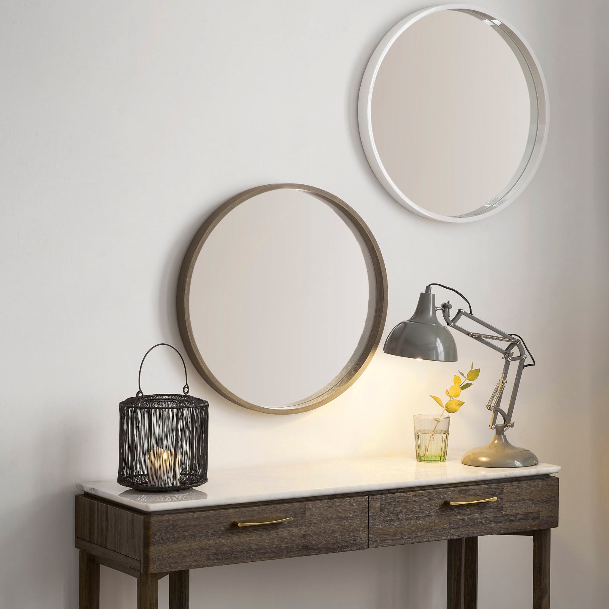 A table with a lamp, candle lantern, and plant is complemented by two Pacific Lifestyle Natural Wood Round Wall Mirrors above, exuding Scandi style charm.