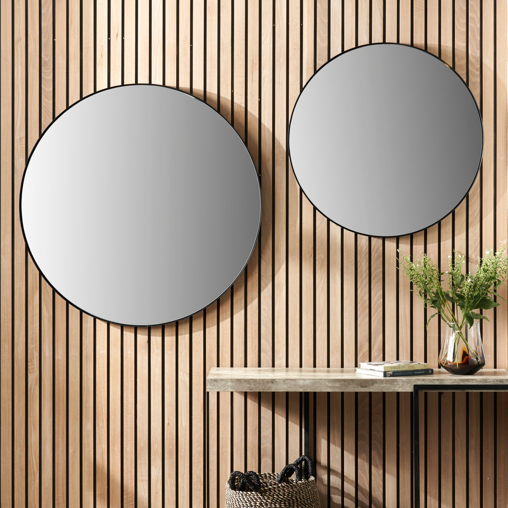 The wooden slatted wall features two Pacific Lifestyle Black Metal Slim Frame Round Wall Mirrors. Below, a console table with a vase of flowers and arranged books creates a harmonious and stylish vignette.
