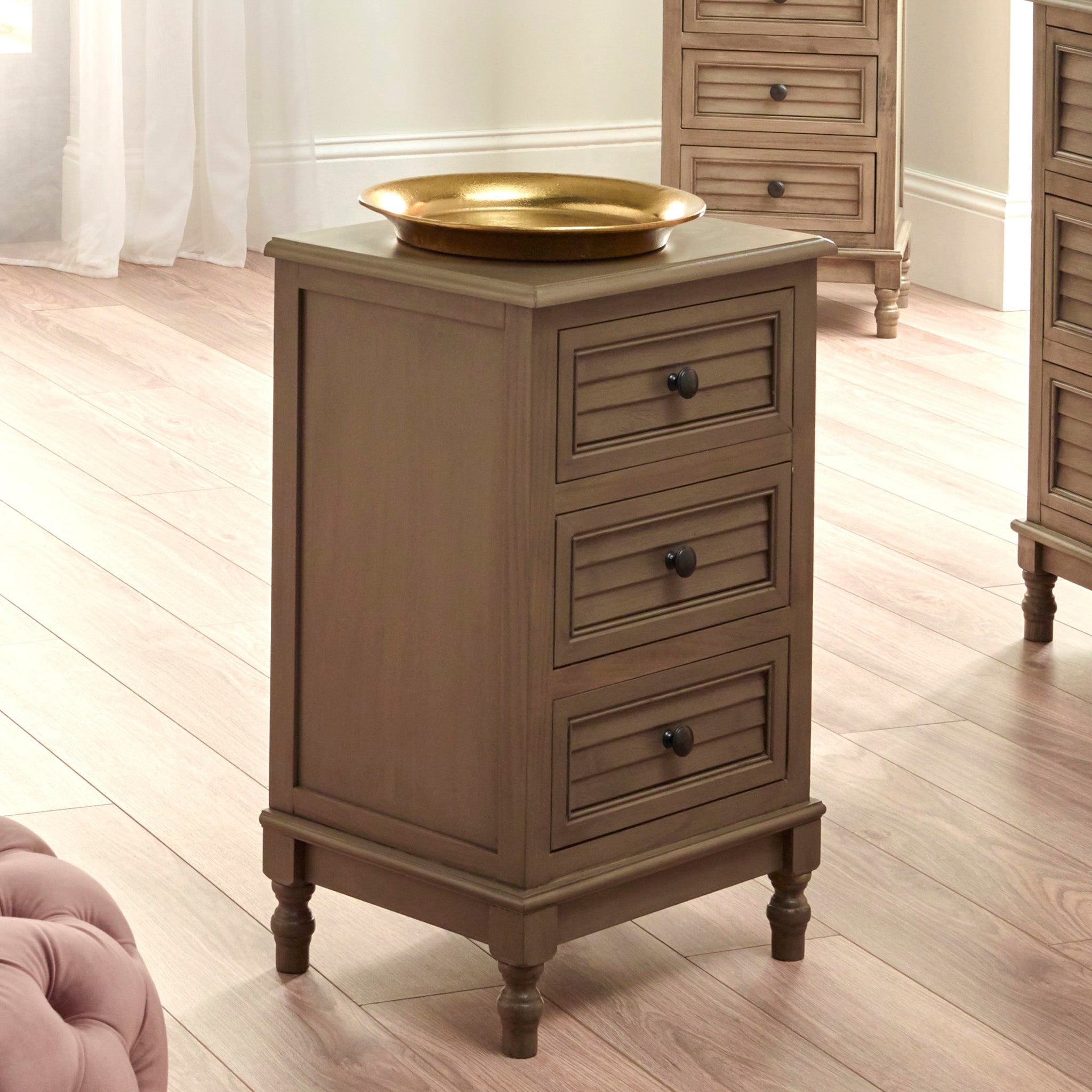 This Pacific Lifestyle Ashwell Taupe Pine 3 Drawer Wood Unit features a taupe finish with a round gold tray on top, elegantly placed on a light wood floor.