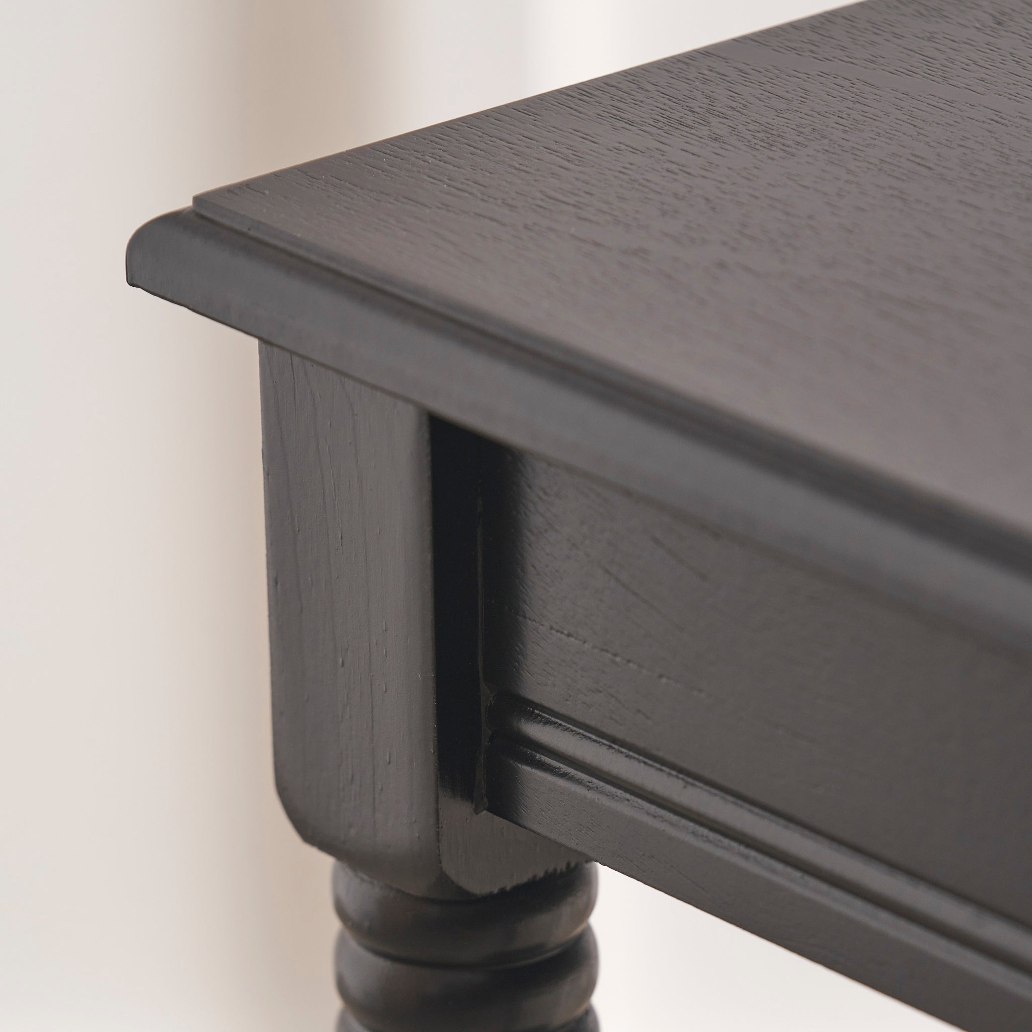 Close-up of a corner of the Heritage Black Pine Wood Accent Table by Pacific Lifestyle, showcasing its ornate turned legs against a light background.