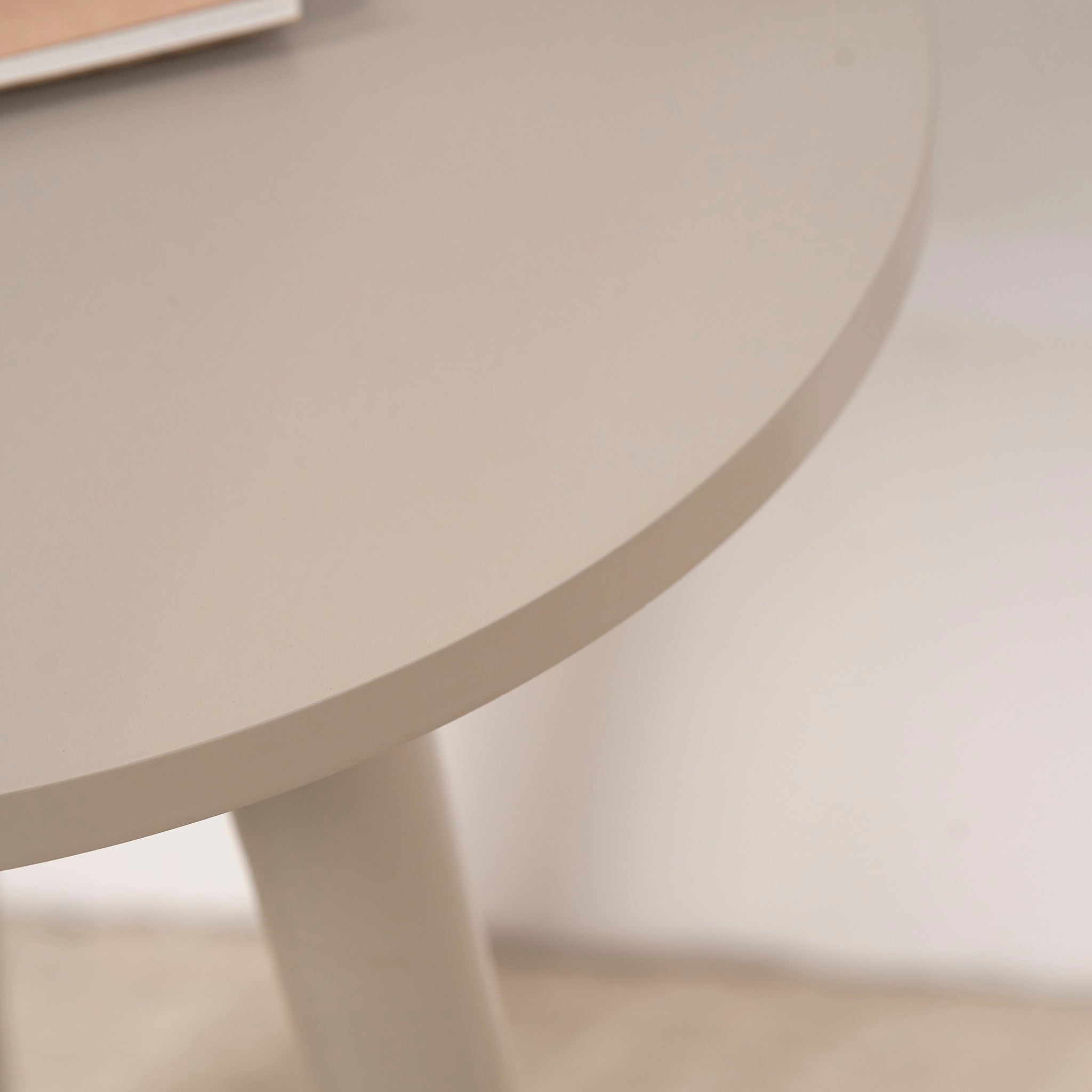 Close-up of the Pacific Lifestyle Devonshire Putty Pine Wood Side Table, showcasing its round compact design and slightly angled legs, with a book partially visible atop its beige surface.