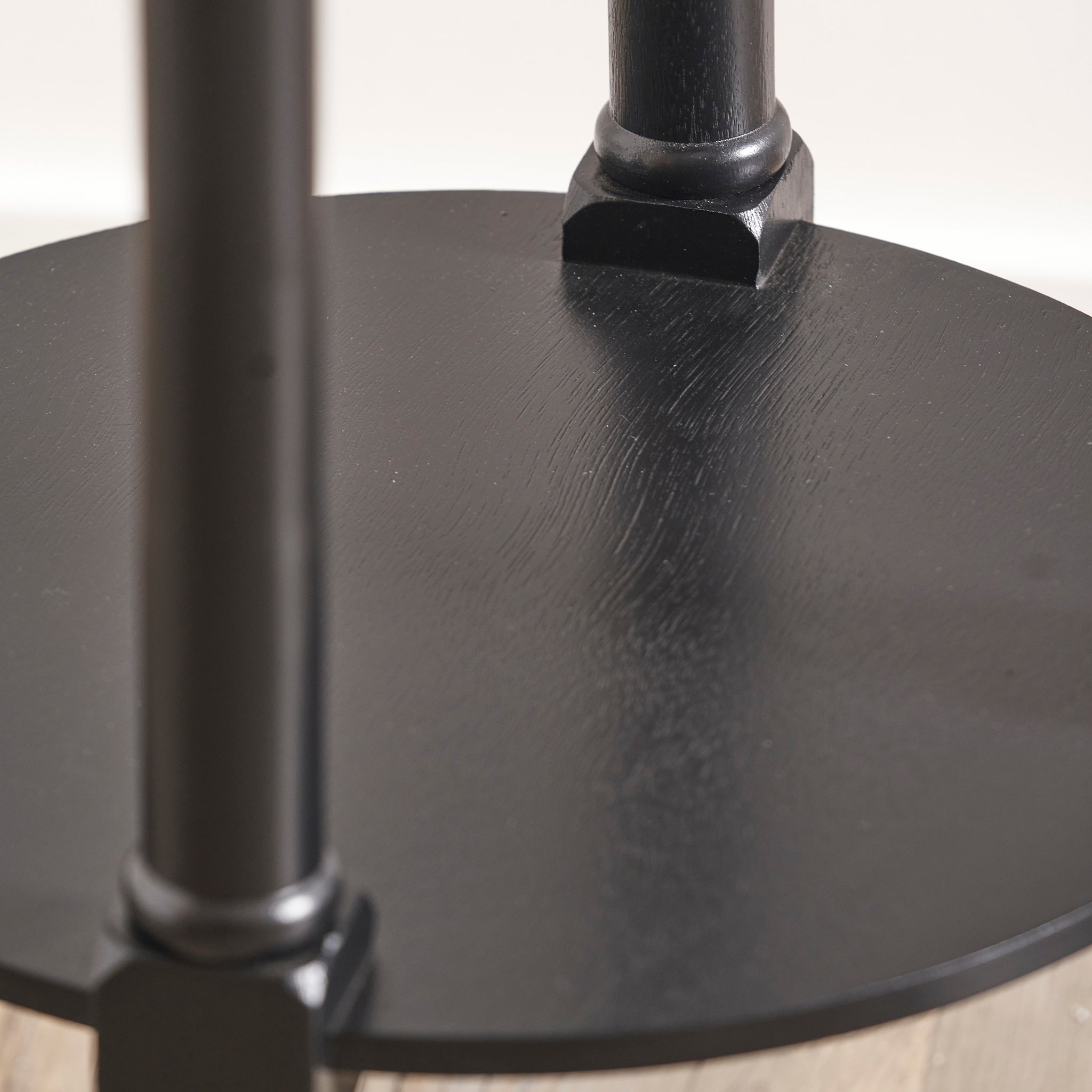 A close-up of the Pacific Lifestyle - Heritage Black Pine Wood Round Accent Table showcases its round design with two vertical supports on a light floor.