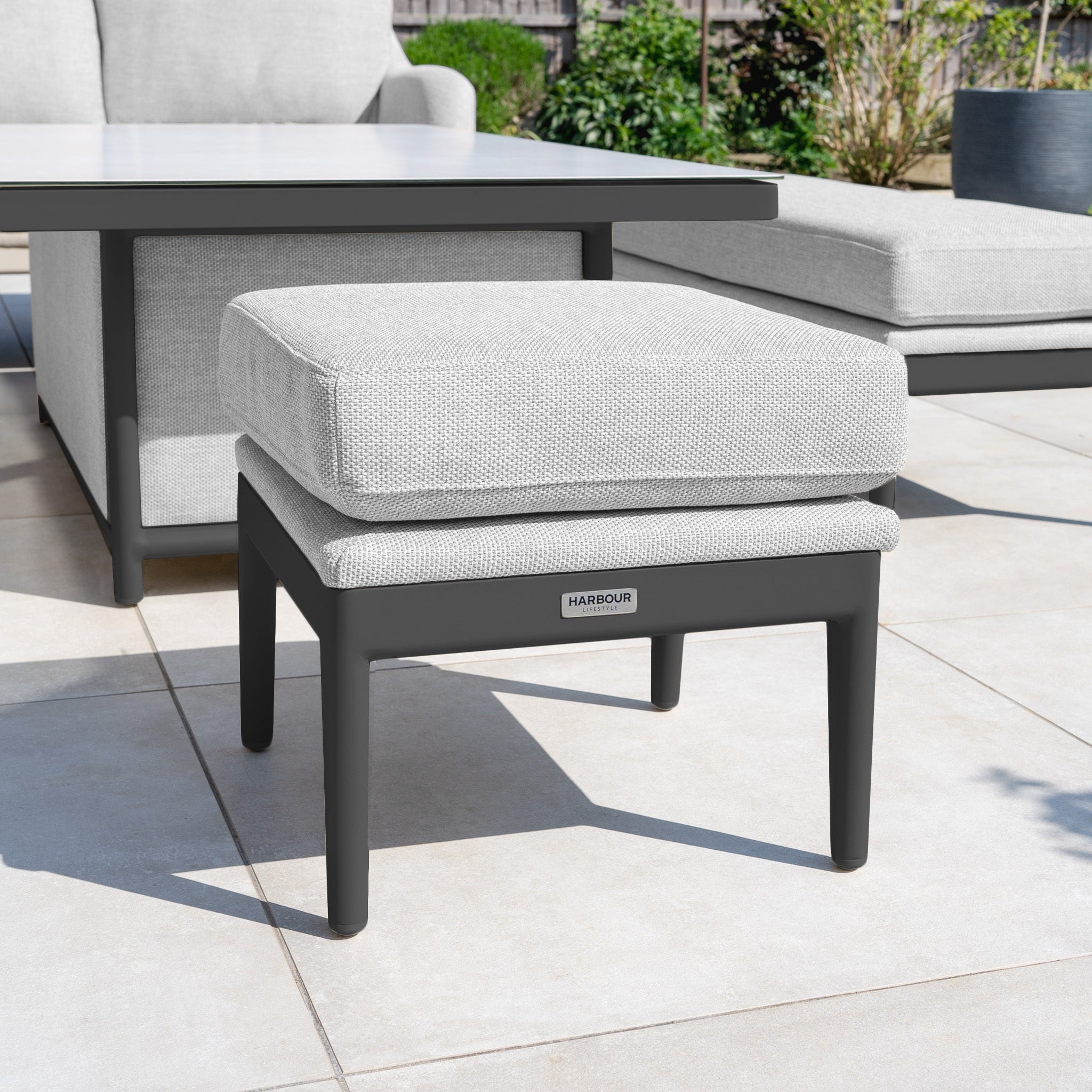 The Luna Stool in Oyster Grey, with quick-dry cushions, sits on a tiled patio among all-weather outdoor furniture and lush plants.