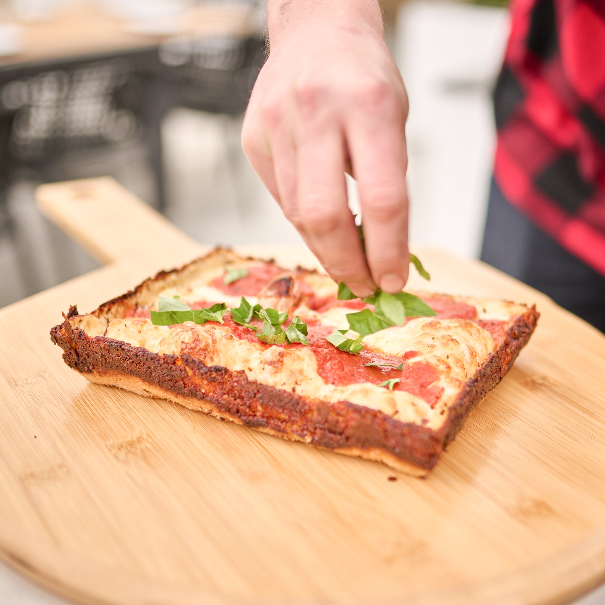 A person garnishes a square pizza with fresh basil leaves on a Bamboo Pizza Board 16", ready for the perfect pizza party.