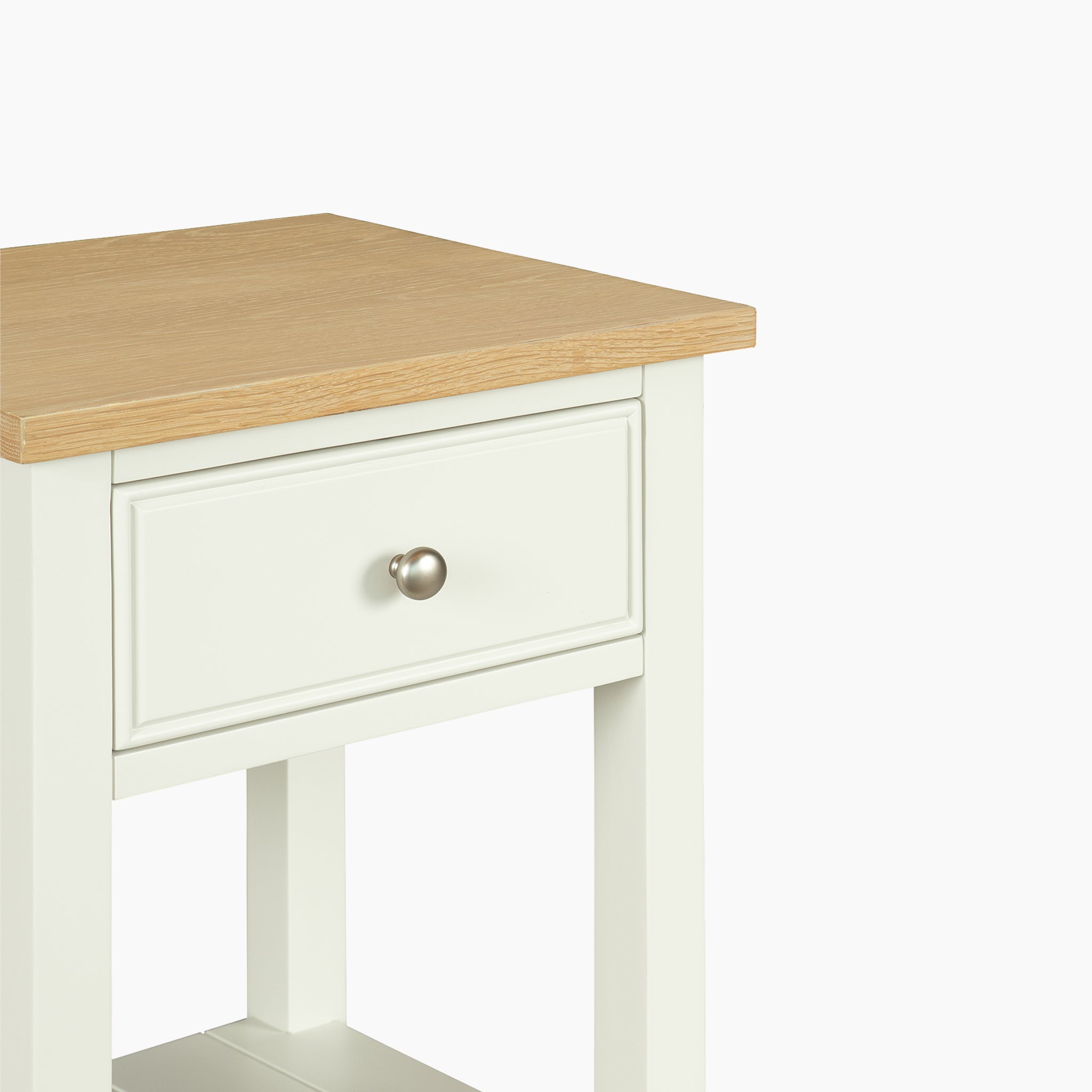 The Amberley Bedside Table in Warm White is ideal for modern country interiors, featuring a white frame, light wood top, and a single drawer with a round silver knob.