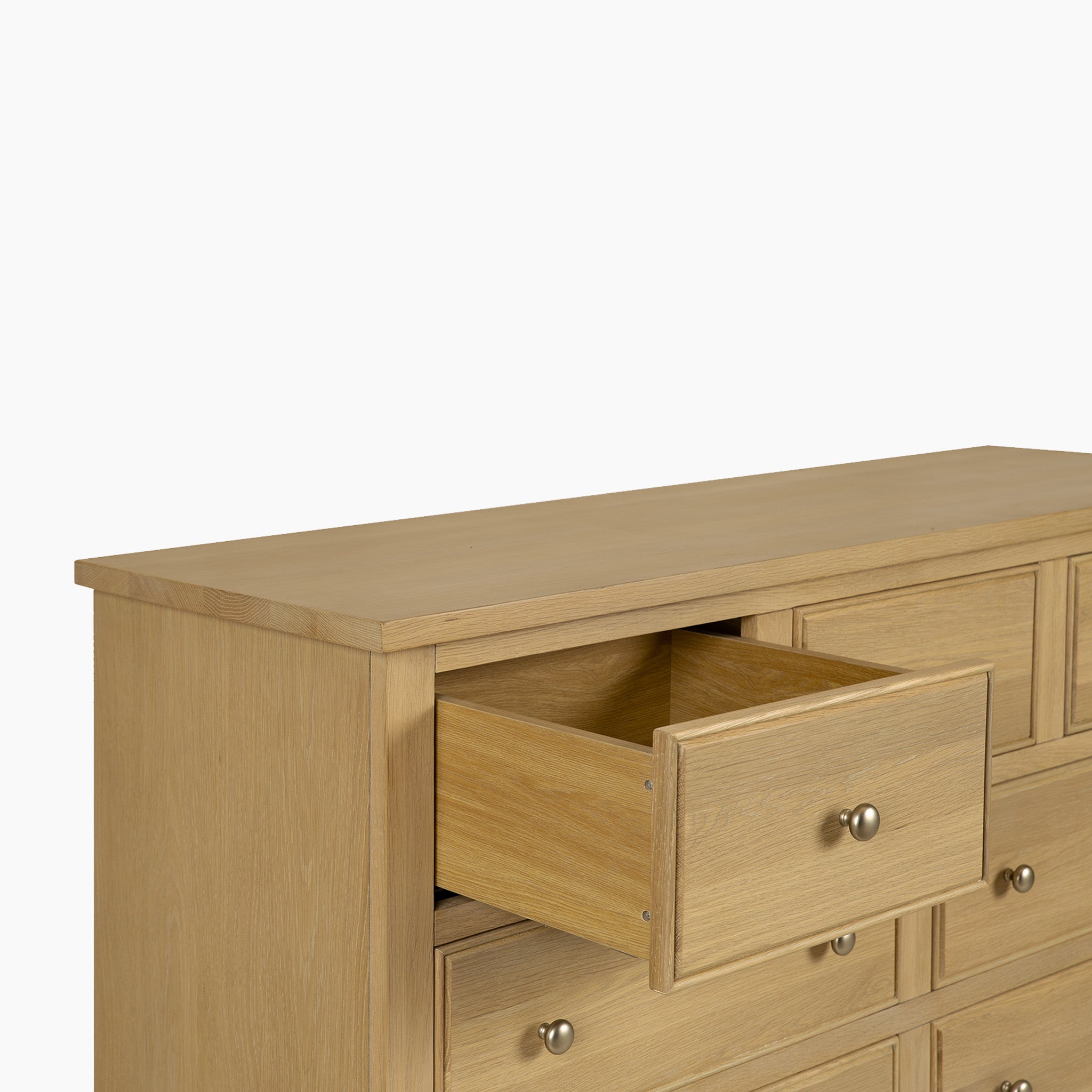 The Amberley 3 Over 4 Chest of Drawers in Light Oak, with multiple drawers including one partially open, provides practical bedroom storage and is shown against a plain white background.