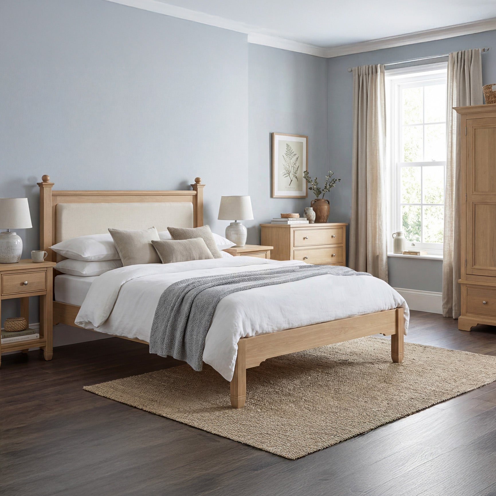 A cozy bedroom with light wood furniture, featuring the Amberley 4ft 6" Double Bed Frame in Light Oak, white bedding, and a large window that fills the space with natural light.