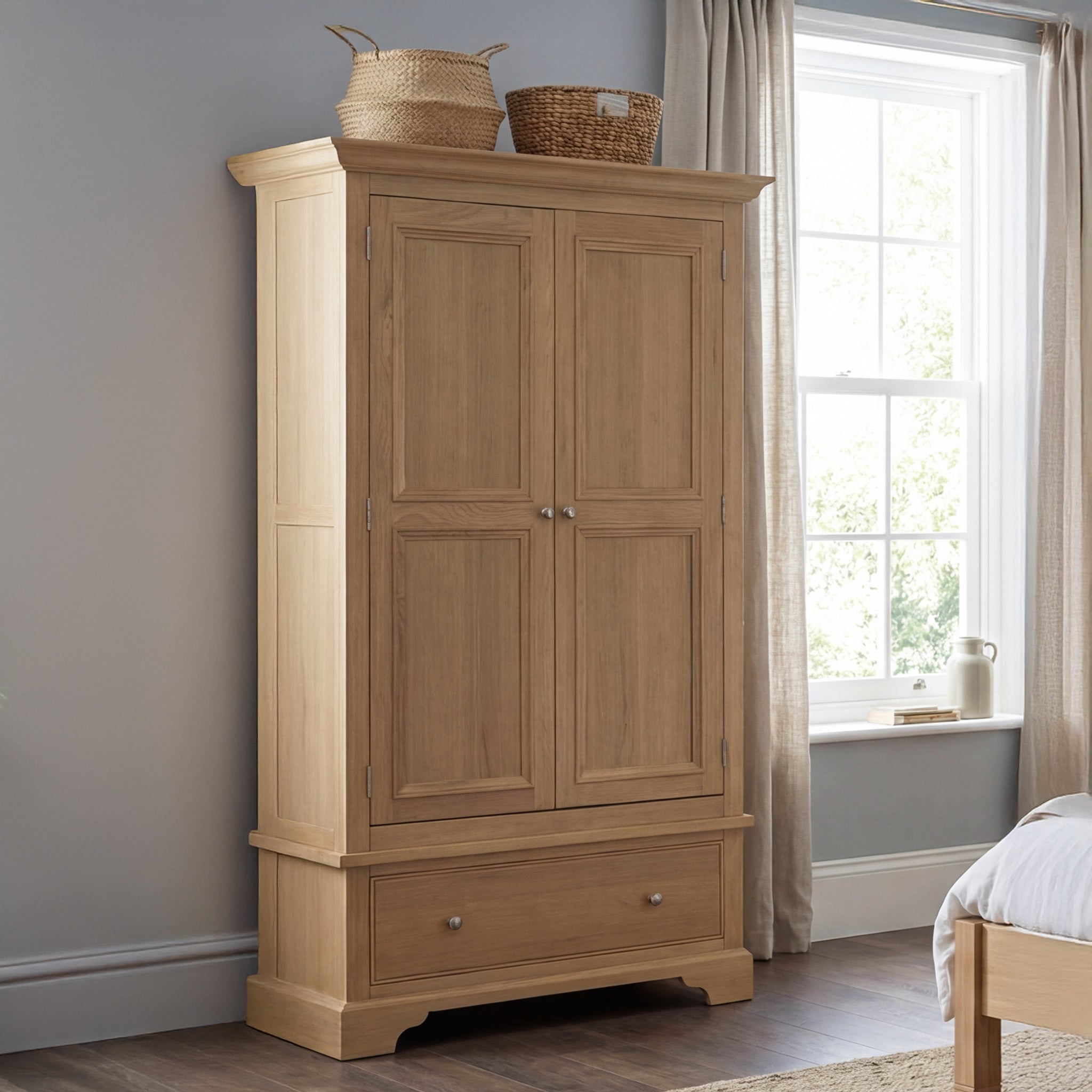 The Amberley Double Wardrobe in Light Oak features a tall design with a spacious drawer, positioned beside a bright bedroom window.