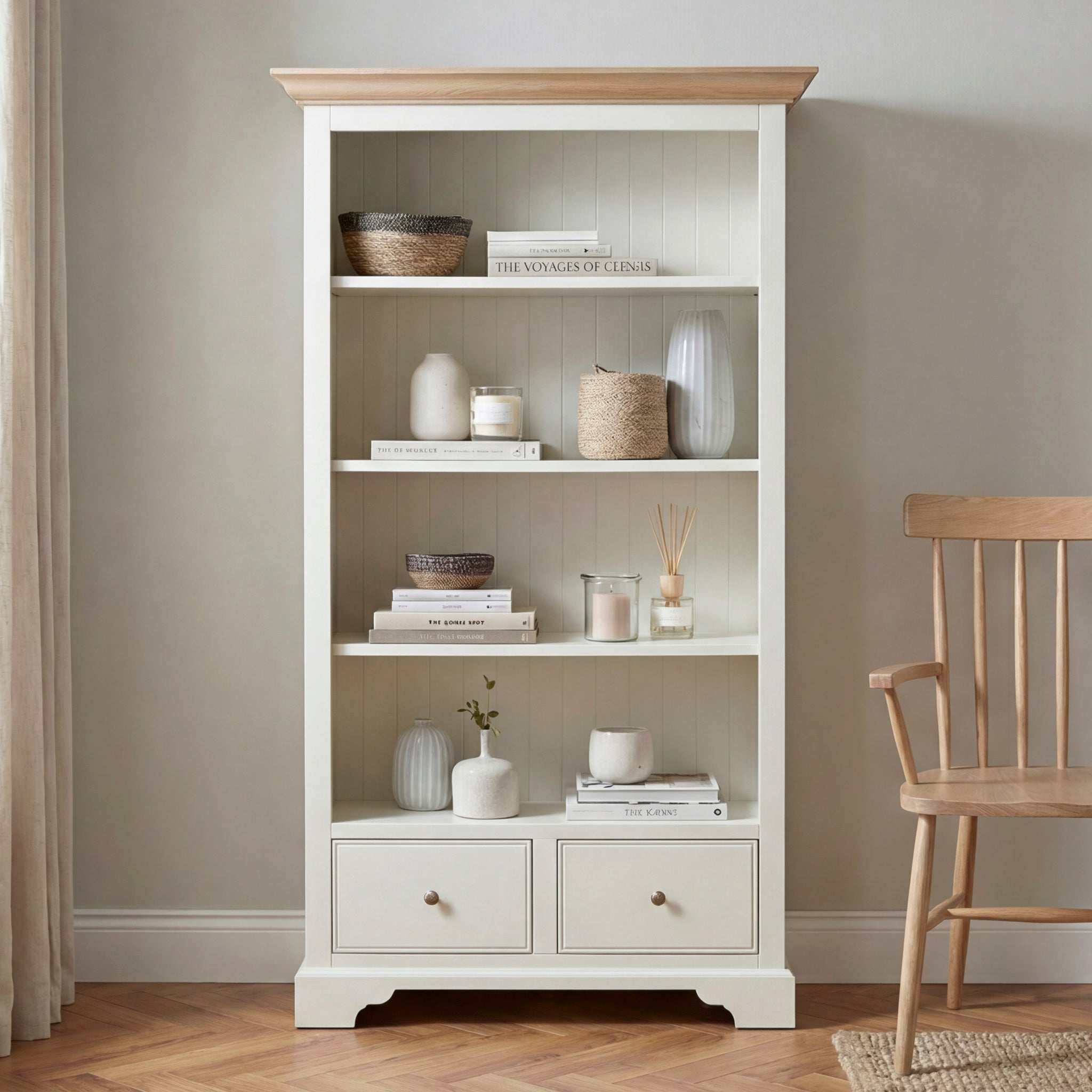 Amberley Large Bookcase in Warm White styled with decor items, books, baskets, vases, and candles beside a wooden chair on a parquet floor.