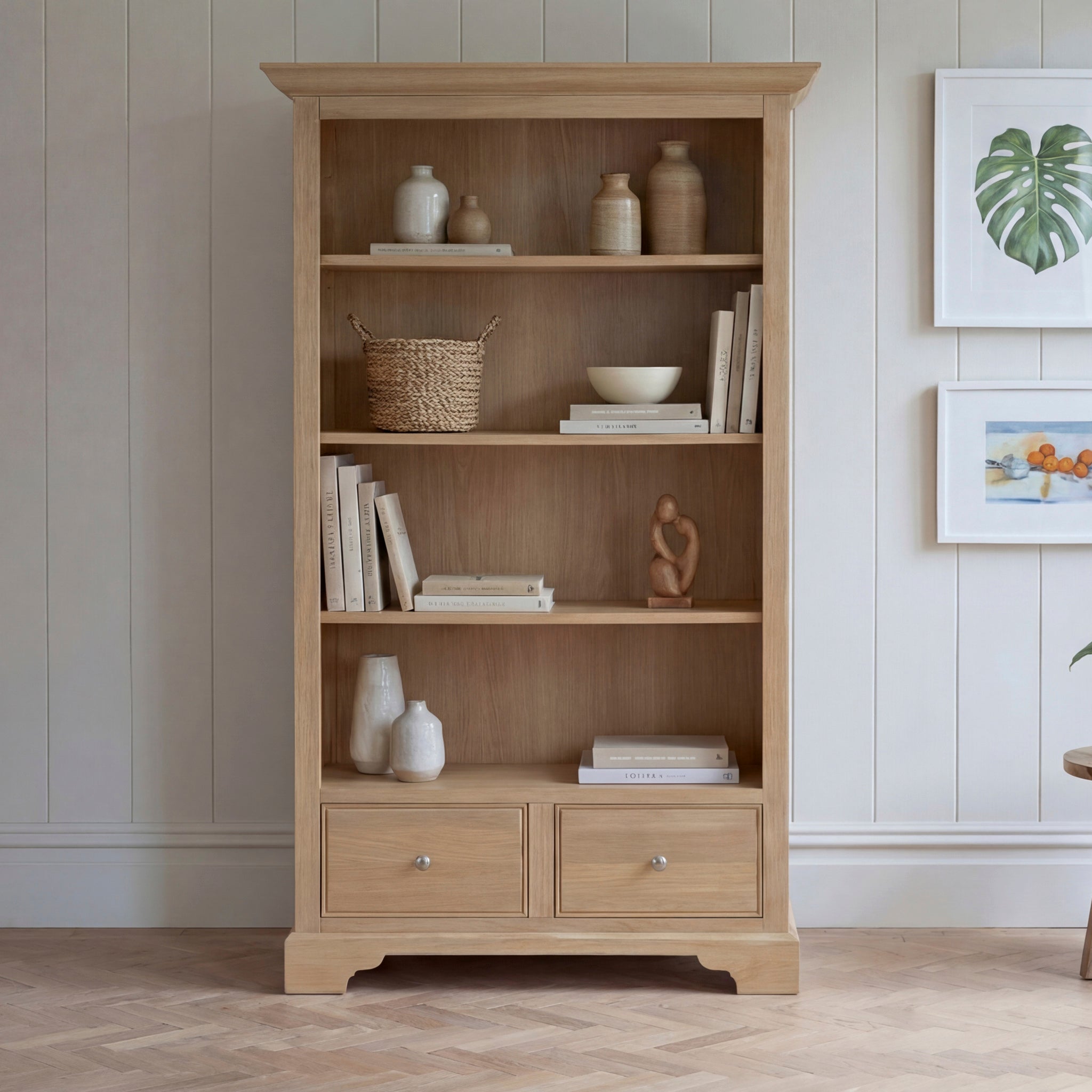 Amberley Large Bookcase in Light Oak, styled with books, ceramic vases, a bowl, basket, and decor accents against a light paneled wall for a charming modern country vibe.