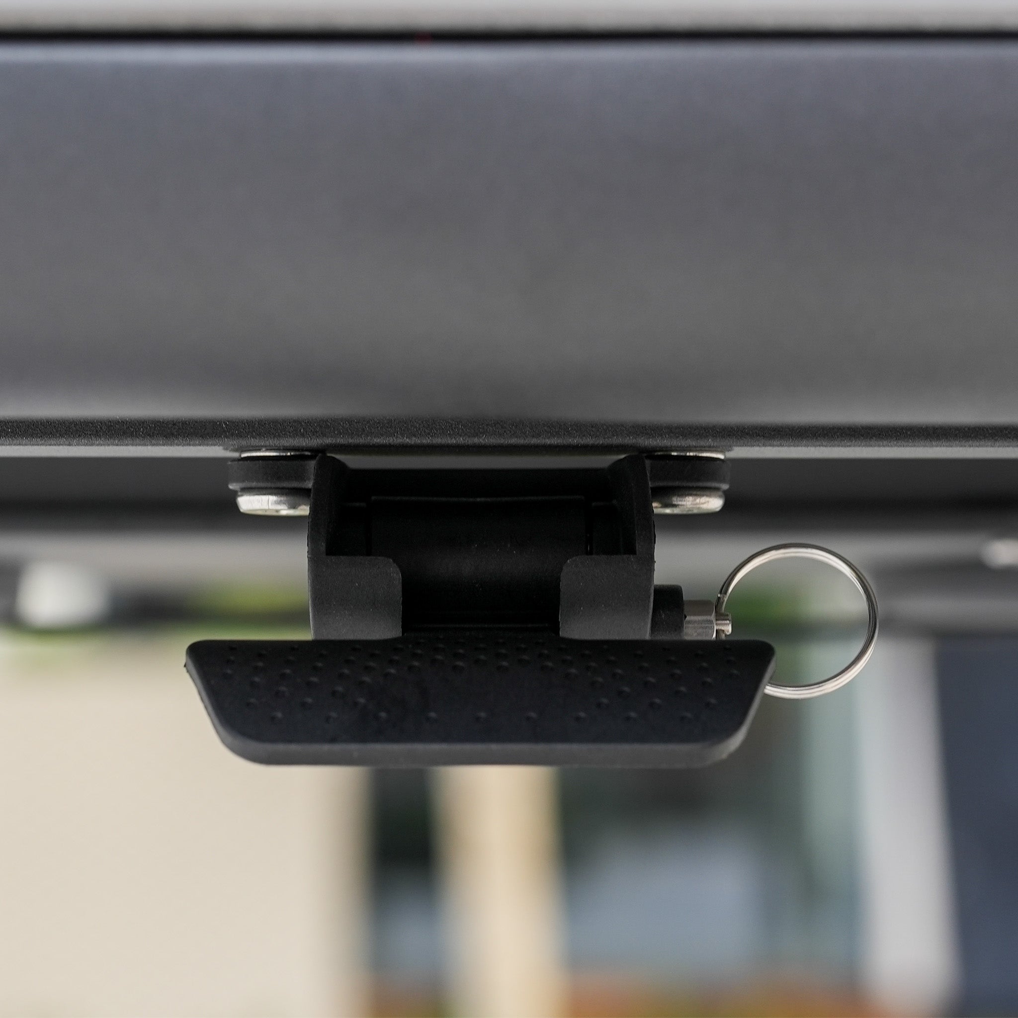 Close-up of a black latch with a metal key ring attached under a gray surface—part of the Luna Outdoor Fabric Large Corner Sofa Set with Altura Rising Table in Oyster Grey, commonly used in modern outdoor furniture.