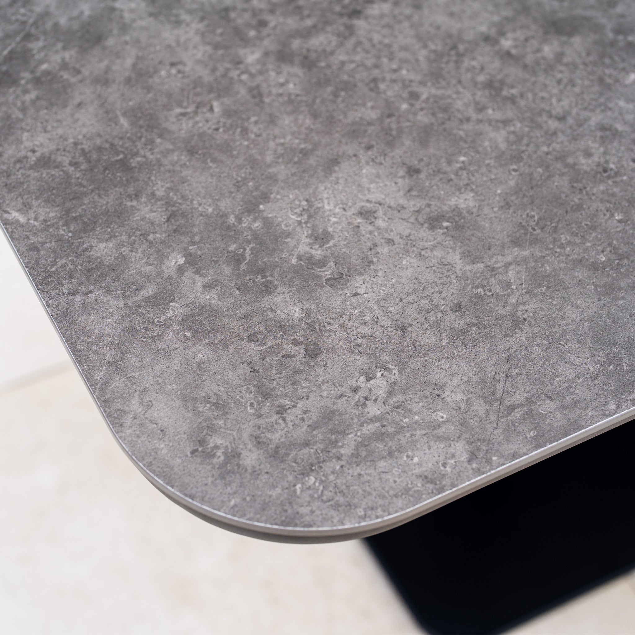 Close-up of the Alva Corner Dining Set with Rising Table and Armchair in Grey (Right Hand), featuring a gray, stone-textured table with rounded corners, perfect for modern gardens or stylish dining areas, set on light floor tiles.