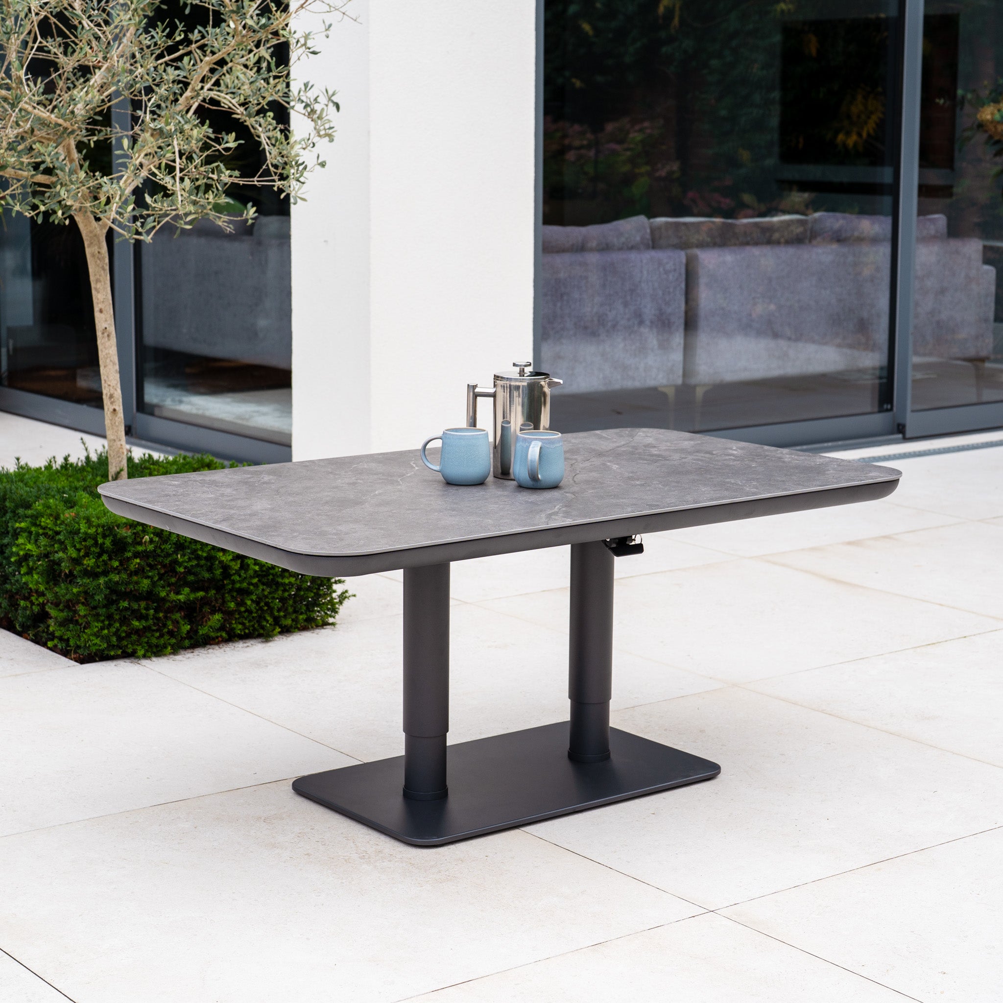 The Luna U-Shape Outdoor Fabric Sofa Set with Altura Rising Table in Grey offers modern garden style, featuring a durable aluminium frame and a sleek table, perfect for your patio near glass doors and lush greenery.