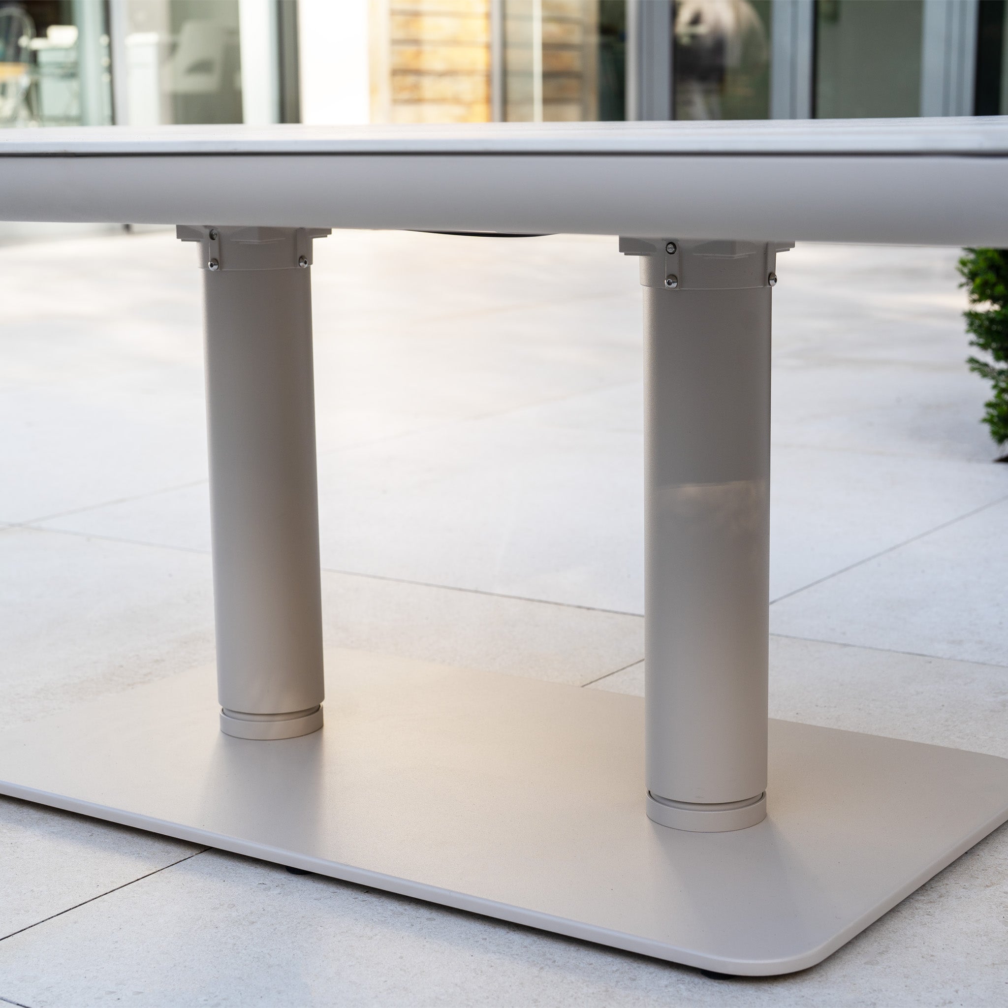 Close-up of the base of the Altura Rising Table from the Pello Deluxe Curved Sofa Set in Fawn, featuring two cylindrical legs on a tiled patio.