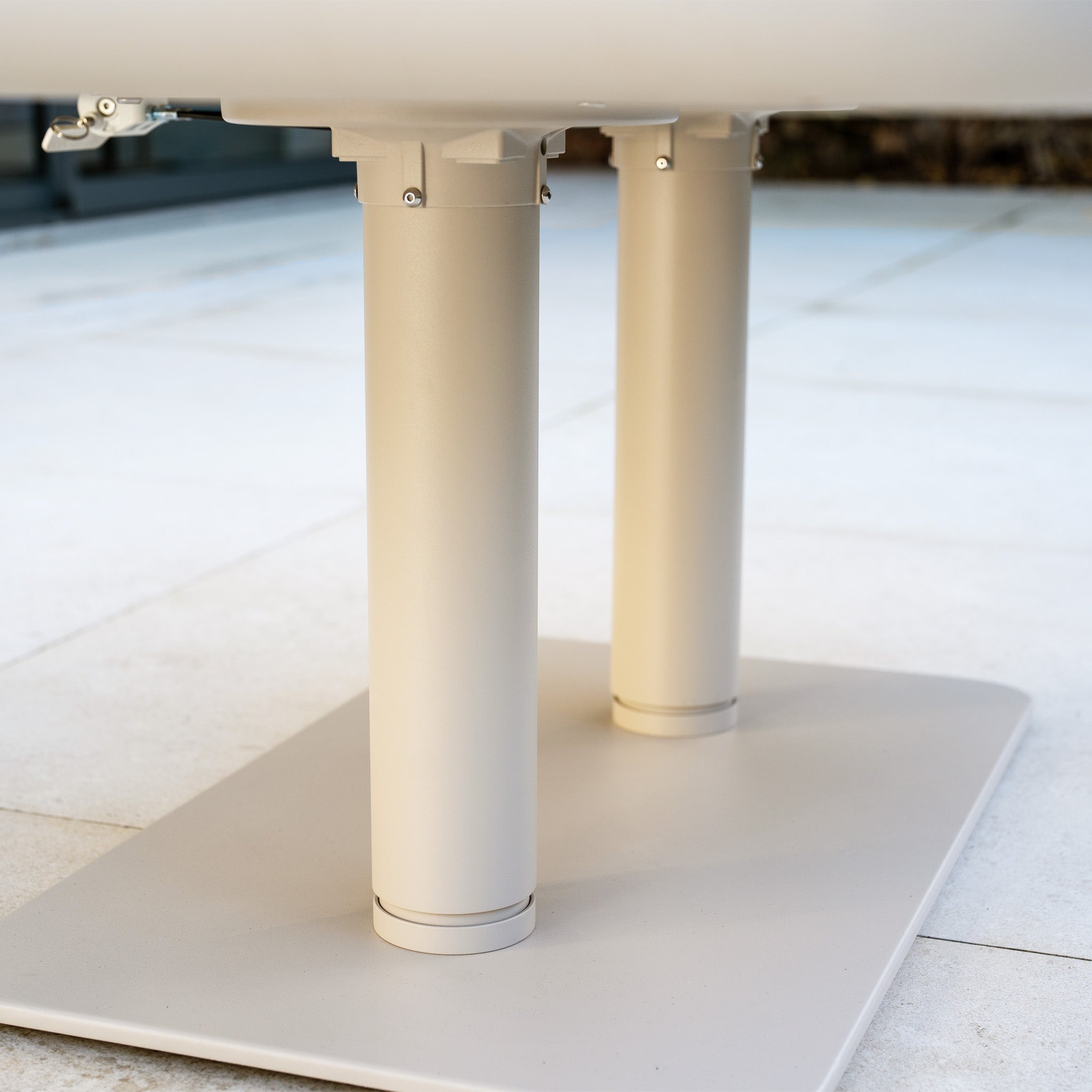 Close-up of two beige cylindrical table legs attached to a flat rectangular base on a tiled floor, part of the Altura Rising Table from the Como Corner Sofa Set with Altura Rising Table in Oatmeal.