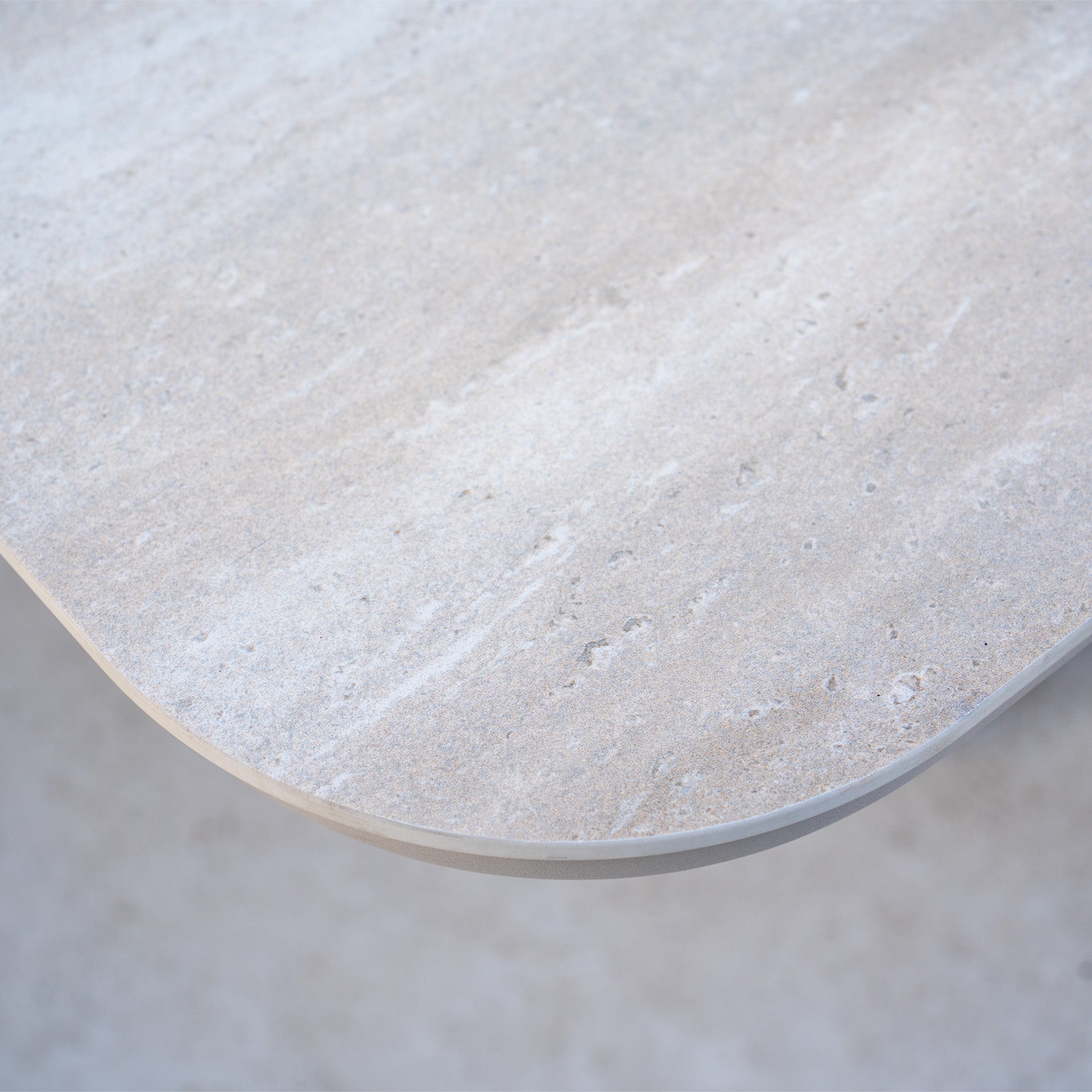 A close-up of a light gray stone tabletop with a rounded corner and smooth texture, perfect for pairing with the Pello Deluxe Curved Sofa Set with Altura Rising Table in Fawn.