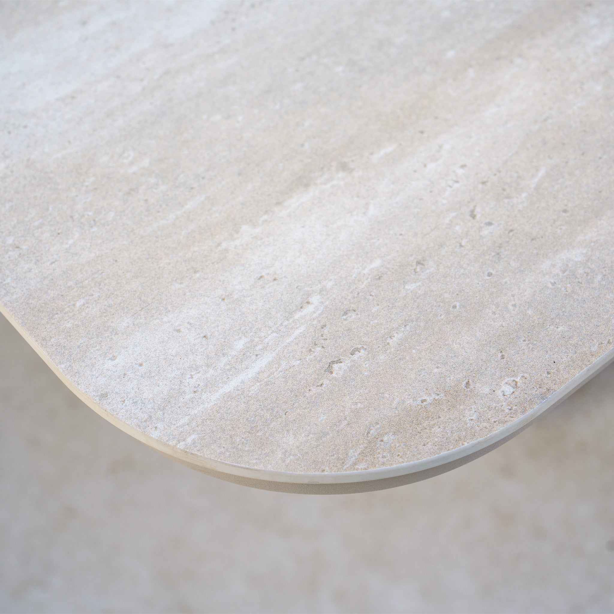 Close-up of the smooth, rounded corner of a light beige stone tabletop with subtle natural patterns, perfectly complementing the Como Corner Sofa Set with Altura Rising Table in Oatmeal for a sophisticated outdoor arrangement.