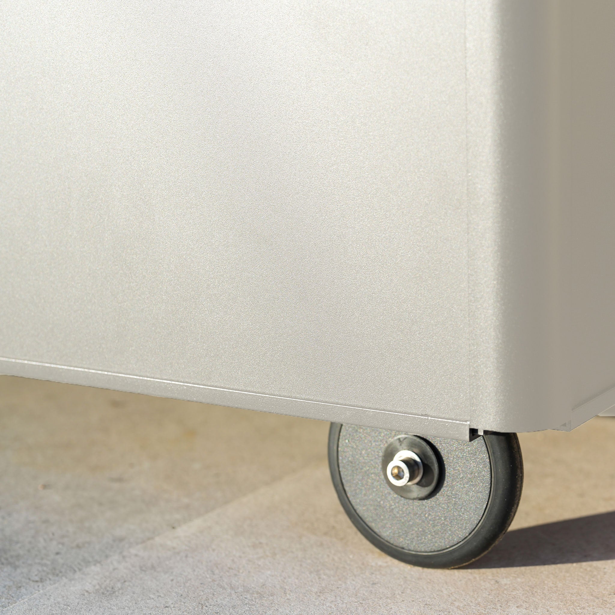 Close-up of a black caster wheel attached to the bottom corner of the Small Aluminium Storage Box in Latte, perfect for outdoor storage.