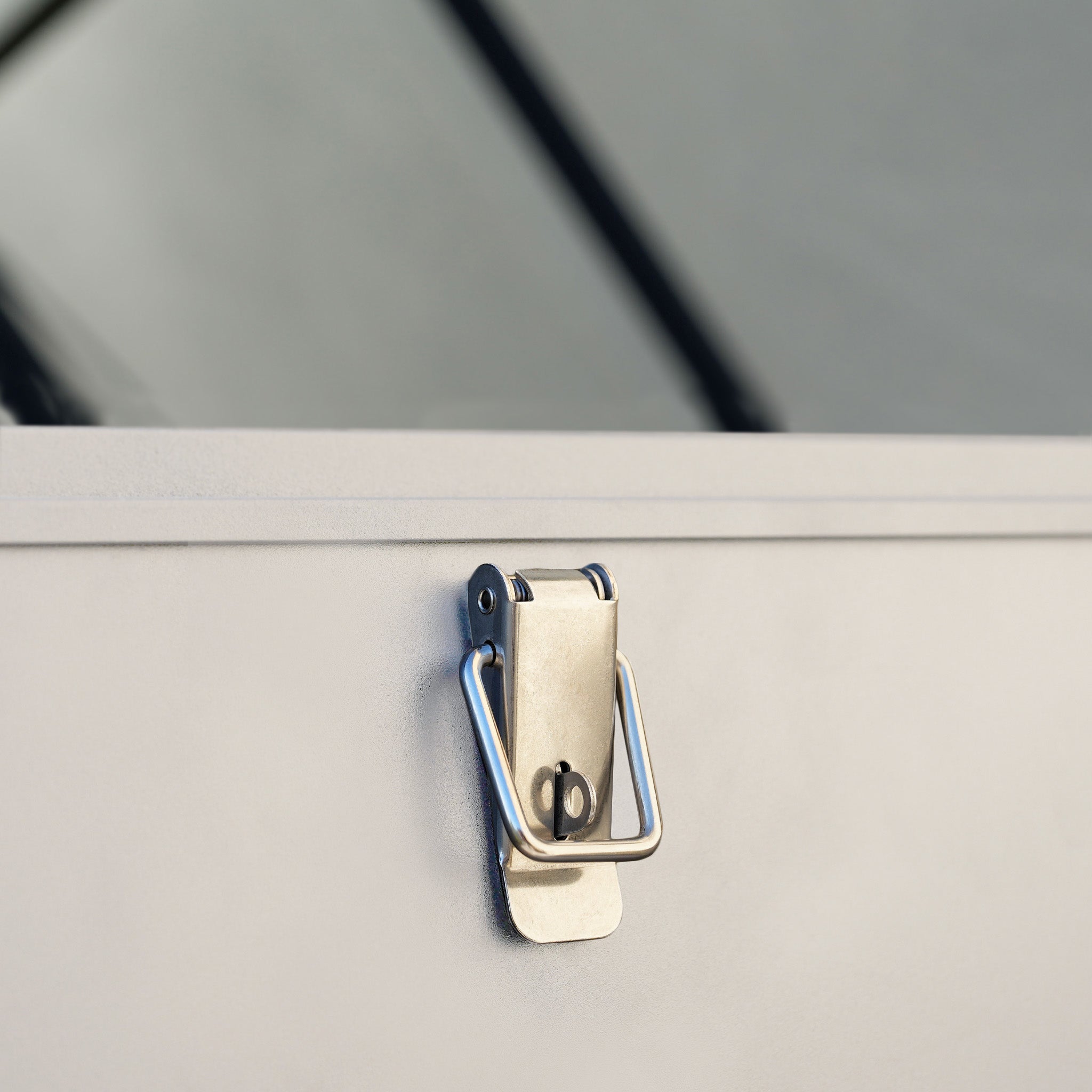 Close-up of the metal latch lock on the Small Aluminium Storage Box in Latte, with a blurred background.